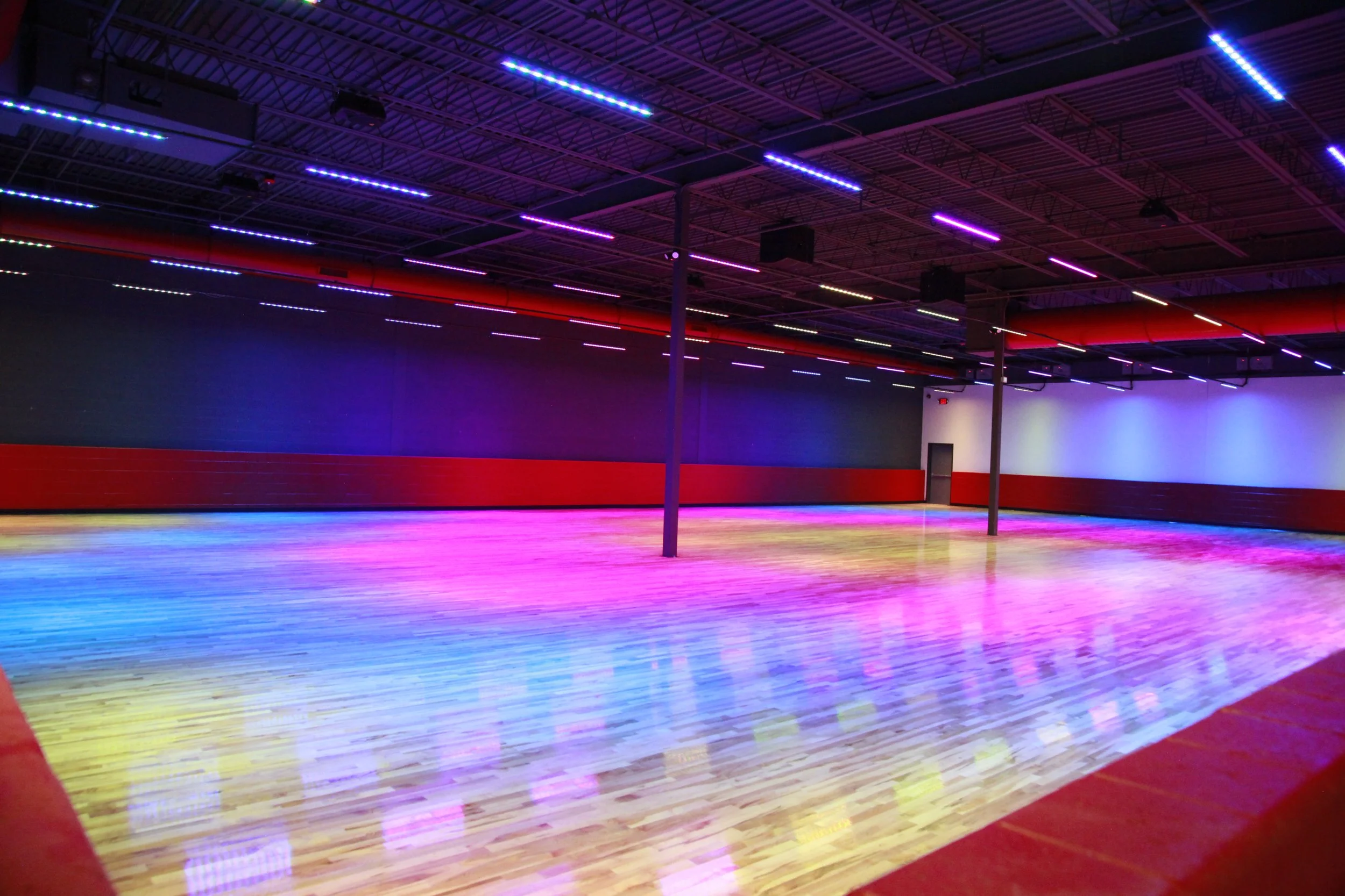 Colorful indoor roller skating rink with rainbow-colored LED lights on the ceiling and wooden floor.