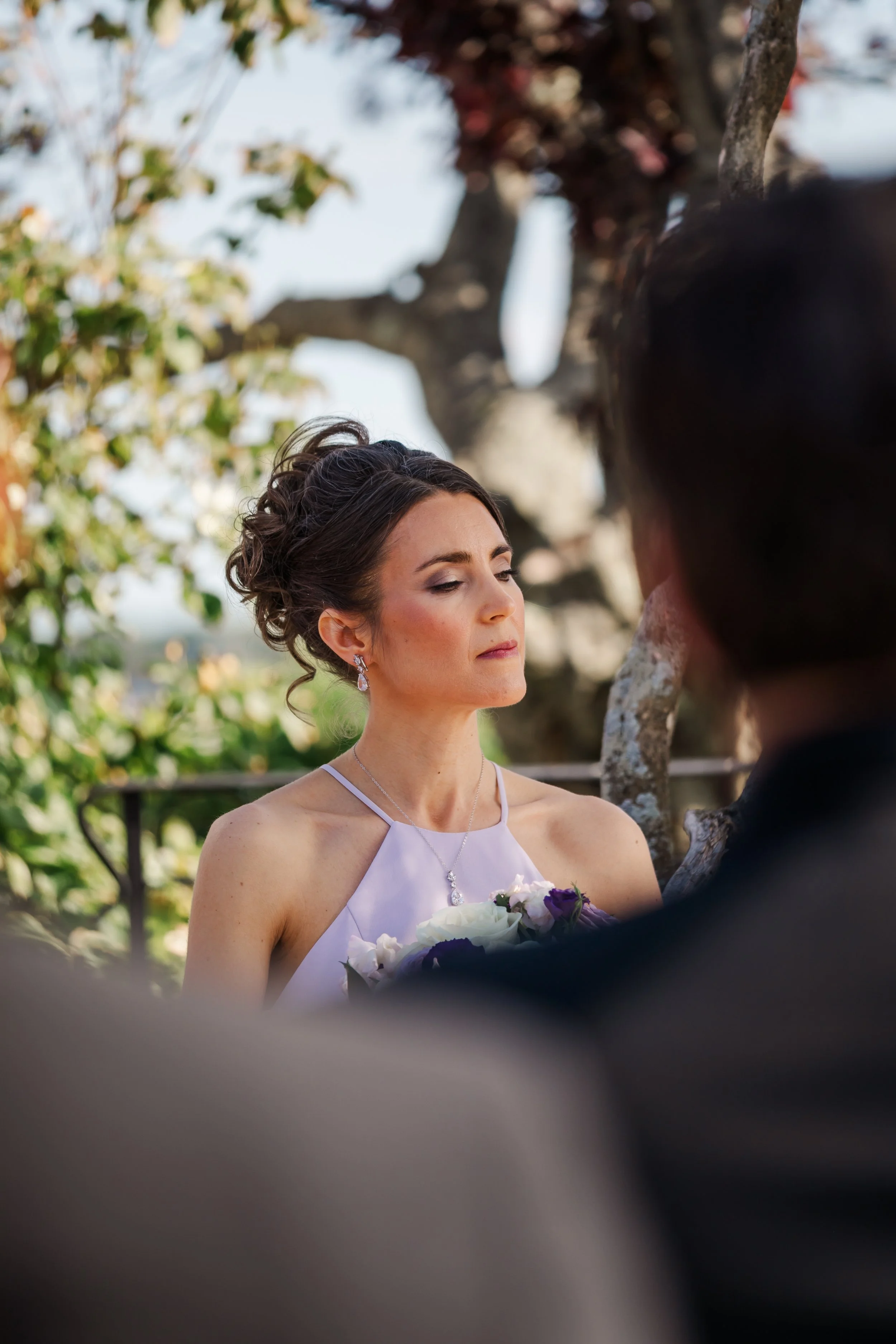 A woman with dark hair and light skin has her makeup done while a makeup artist applies eye makeup with a brush.