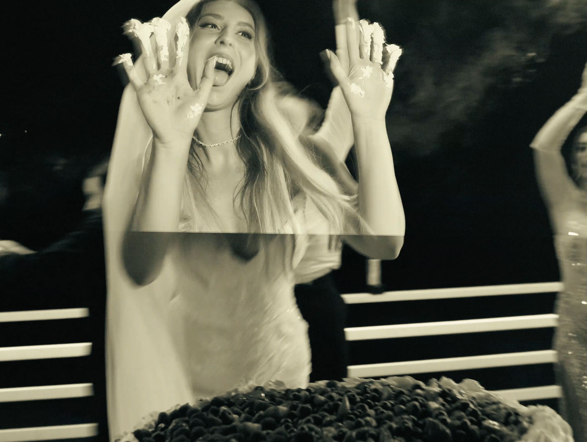 A woman with long hair and a dress, seemingly excited, with her mouth open, hands raised, and fingers in a claw-like gesture, standing behind a glass display filled with blueberries.