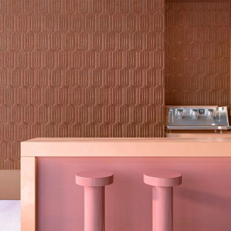 Interior scene with a pink bar counter and two matching pink round stools. In the background, there's a textured brown wall with geometric patterns and a metallic stove with control knobs.