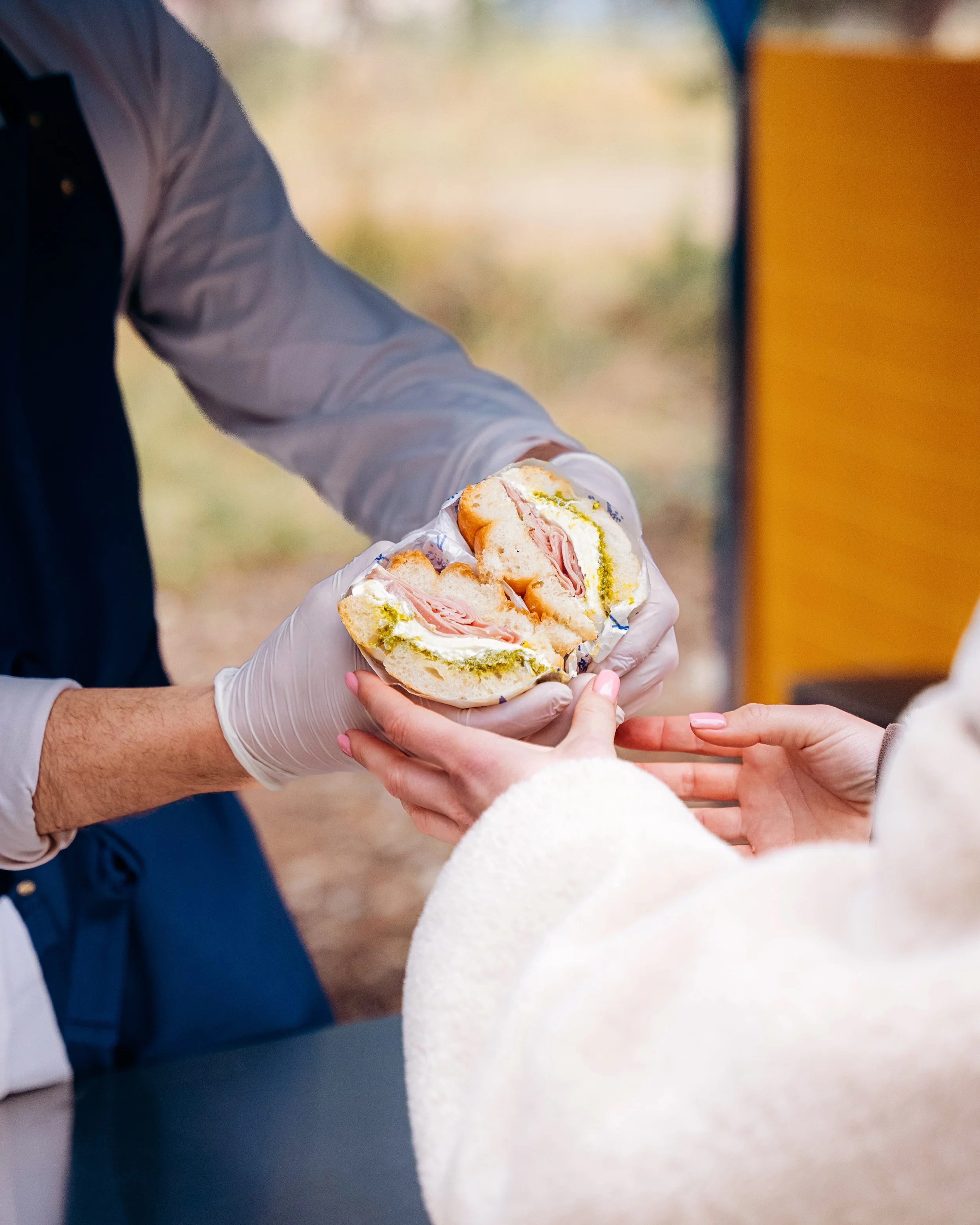 Un sandwich est remis d'une main gantée à une autre personne.