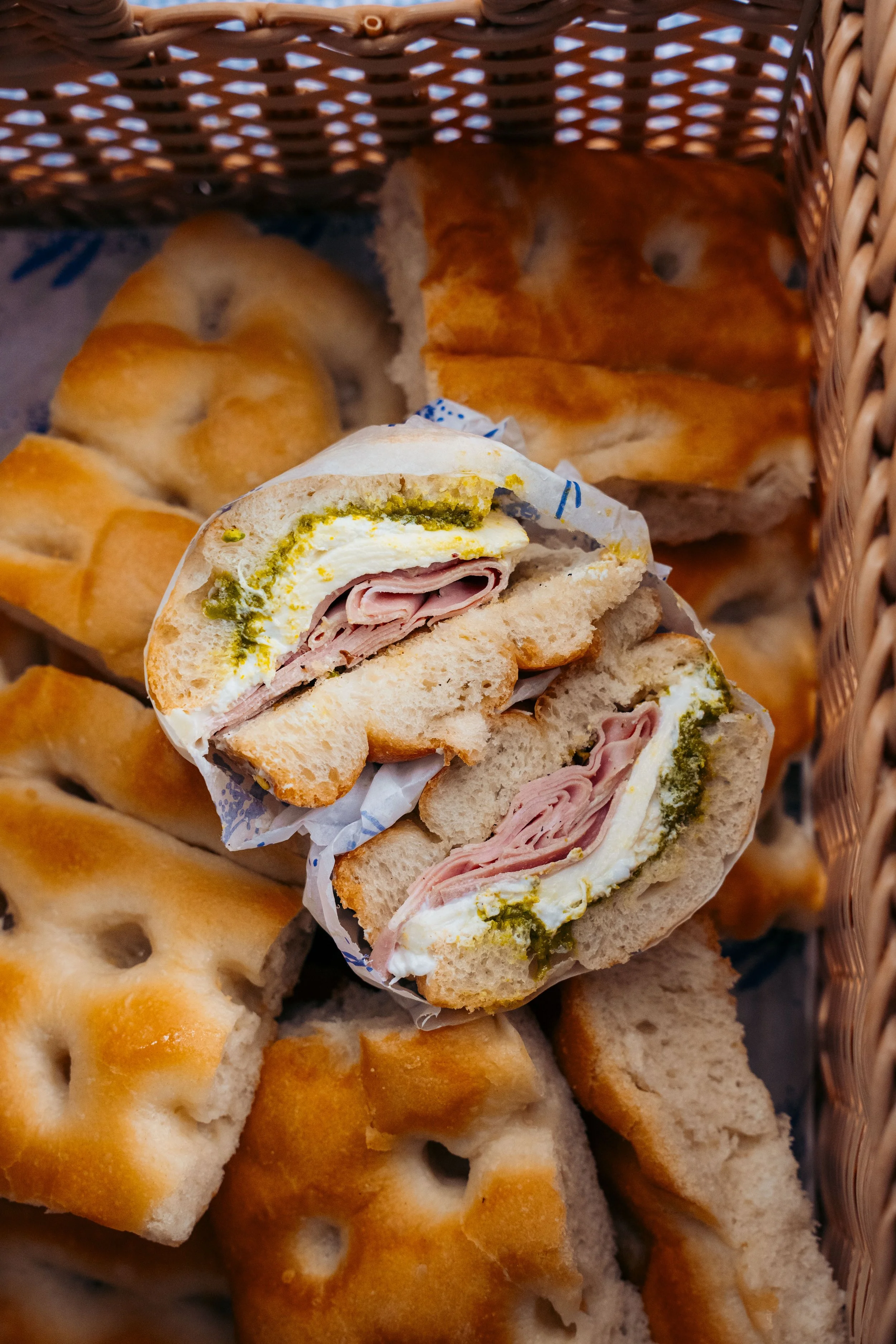 Sandwich avec jambon, fromage, et pesto dans du pain focaccia, présenté dans un panier en osier.