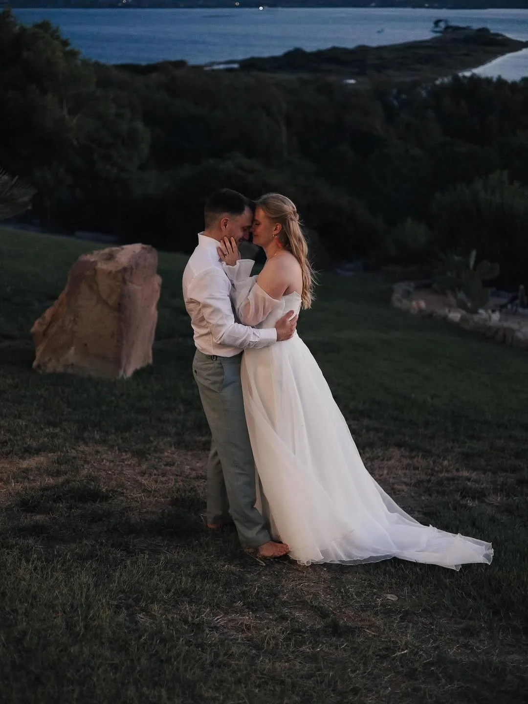 Una coppia di sposi si abbraccia e si bacia sotto il cielo al tramonto, con lo sfondo di una costa con il mare in Sardegna a villa maestrale.