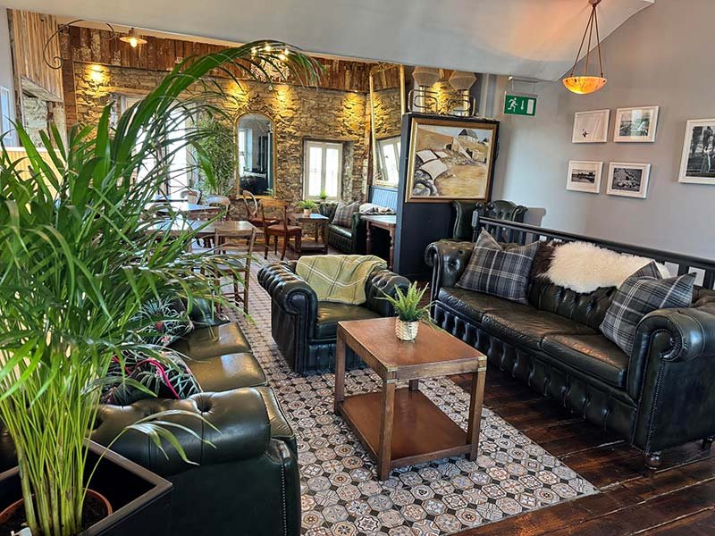 Cozy living room with leather sofas, a wooden coffee table with a potted plant, and brick wall with windows and framed photos.