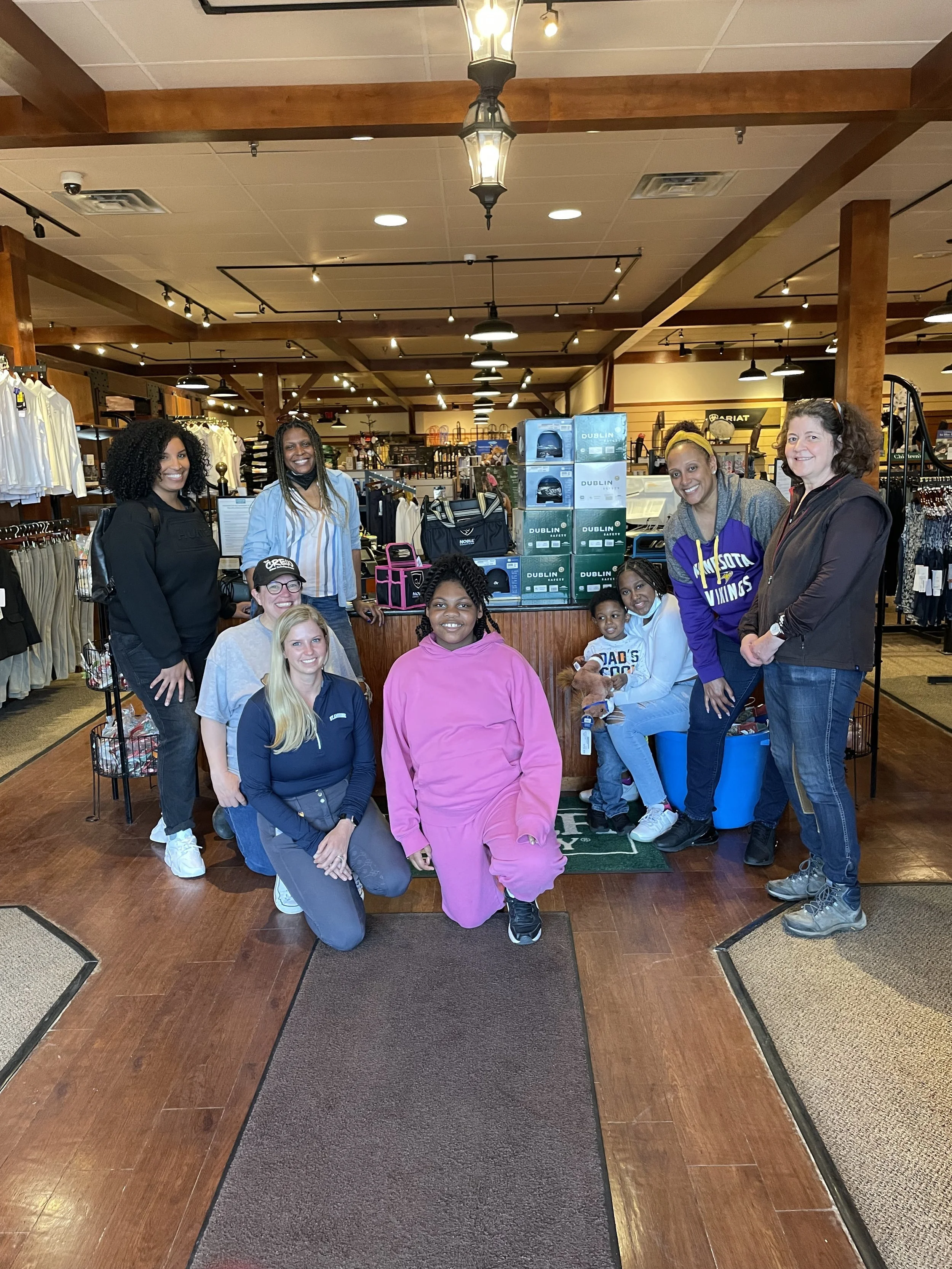 Group of people posing in a clothing store with wood flooring and overhead lights.