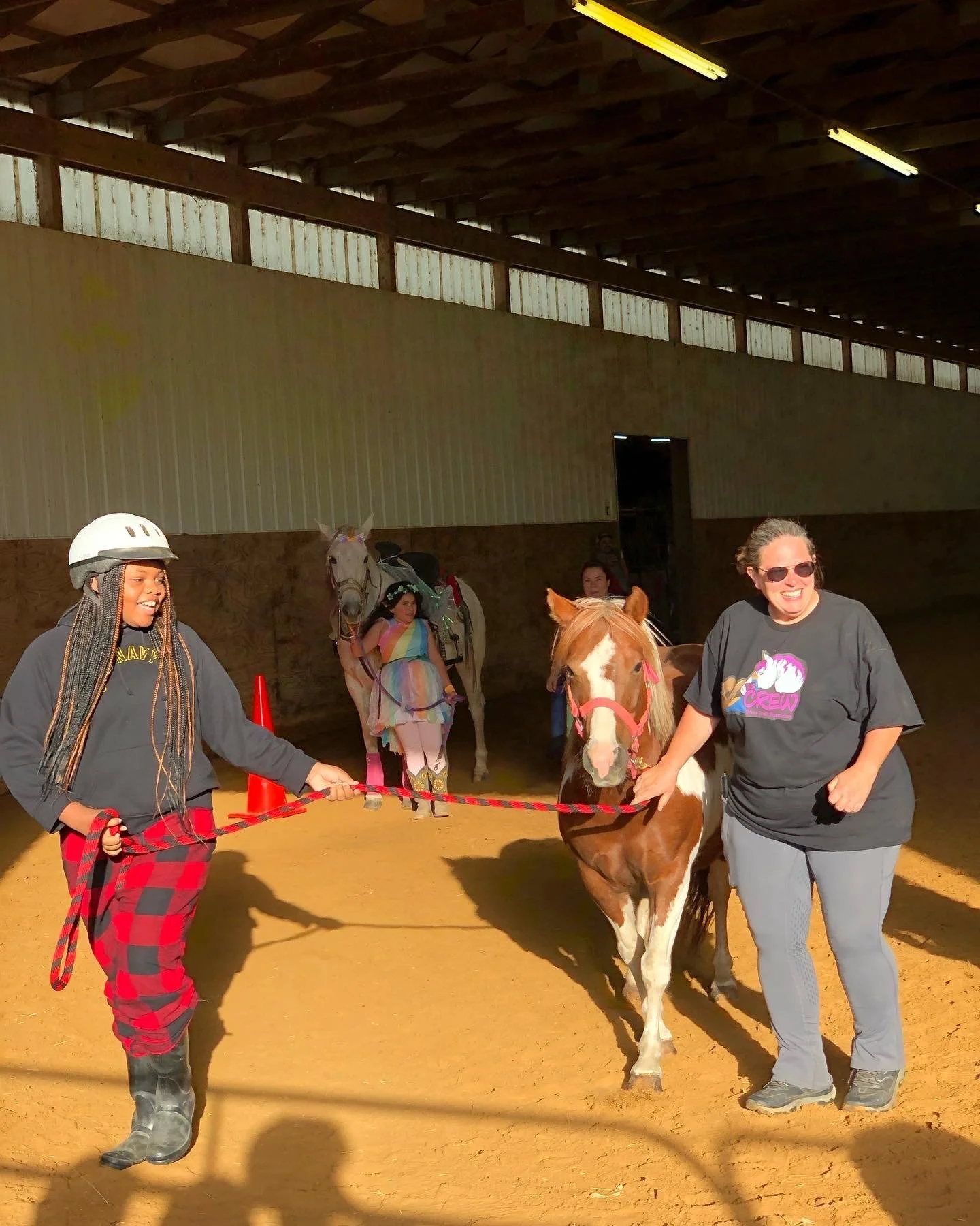 Two women leading a pony indoors with rider in the background