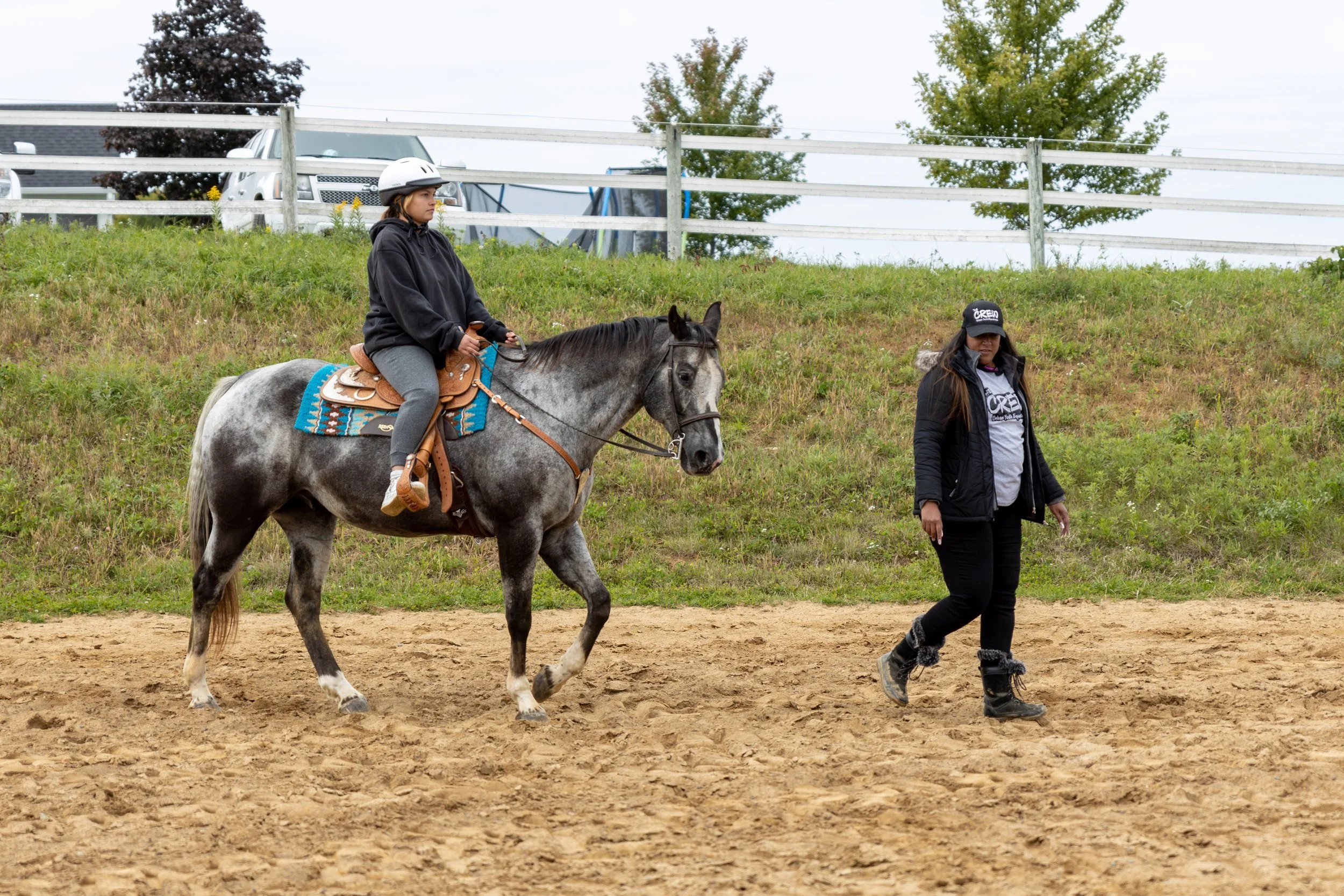 Person riding a horse in an outdoor arena, accompanied by a walking instructor.