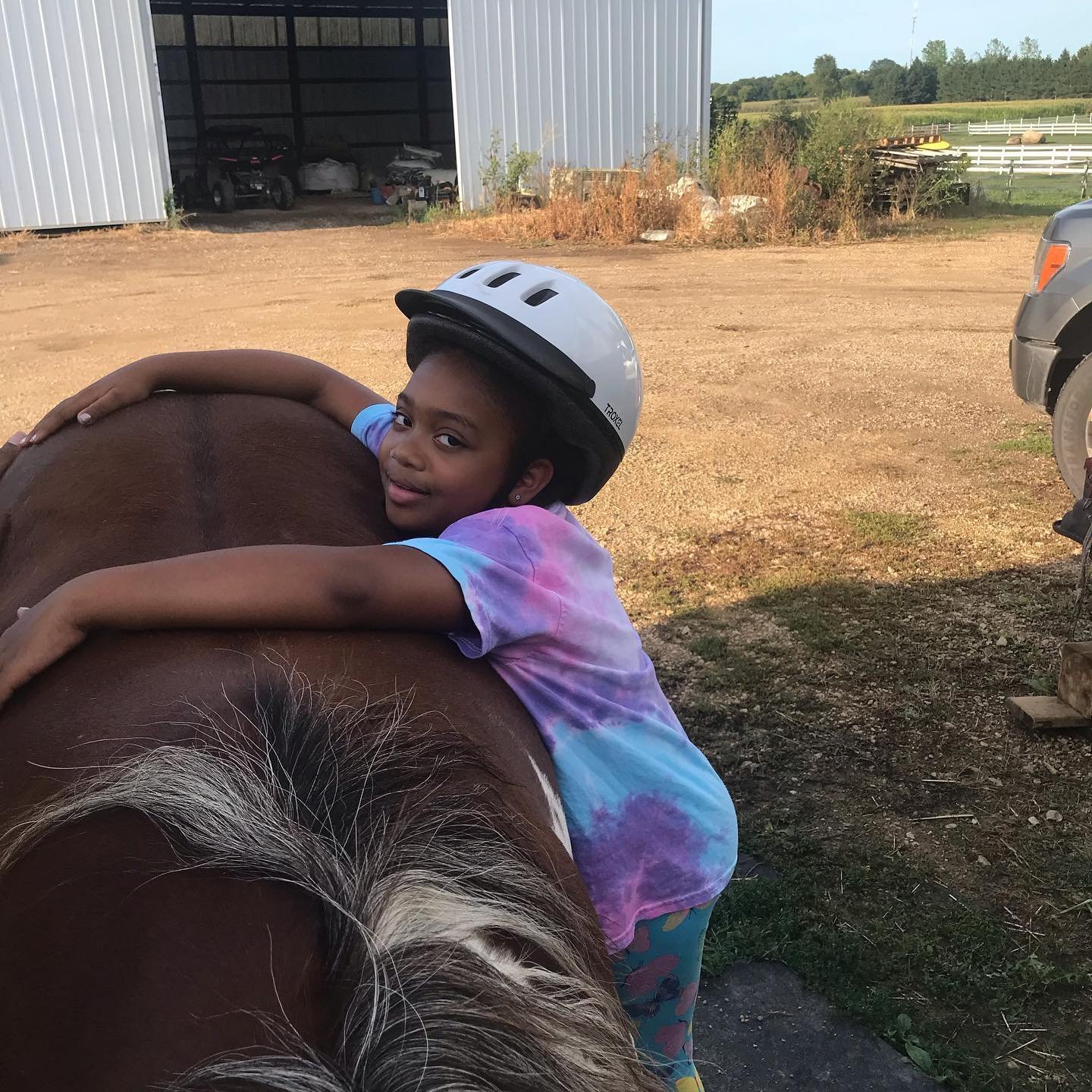 Child in a helmet hugging a horse at a farm