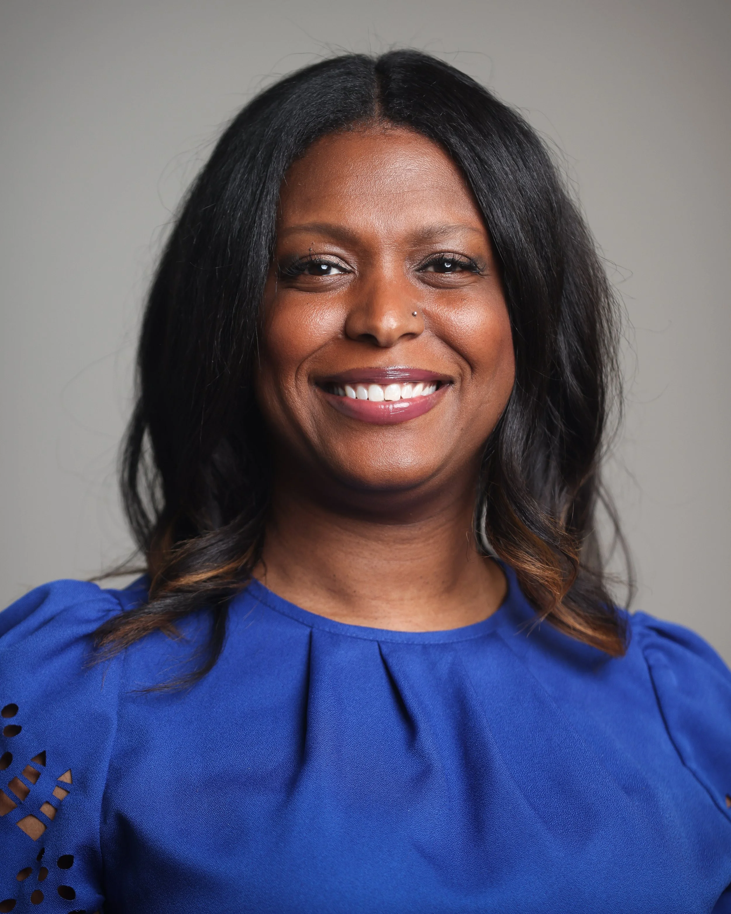 Smiling woman in a blue blouse with a neutral background.