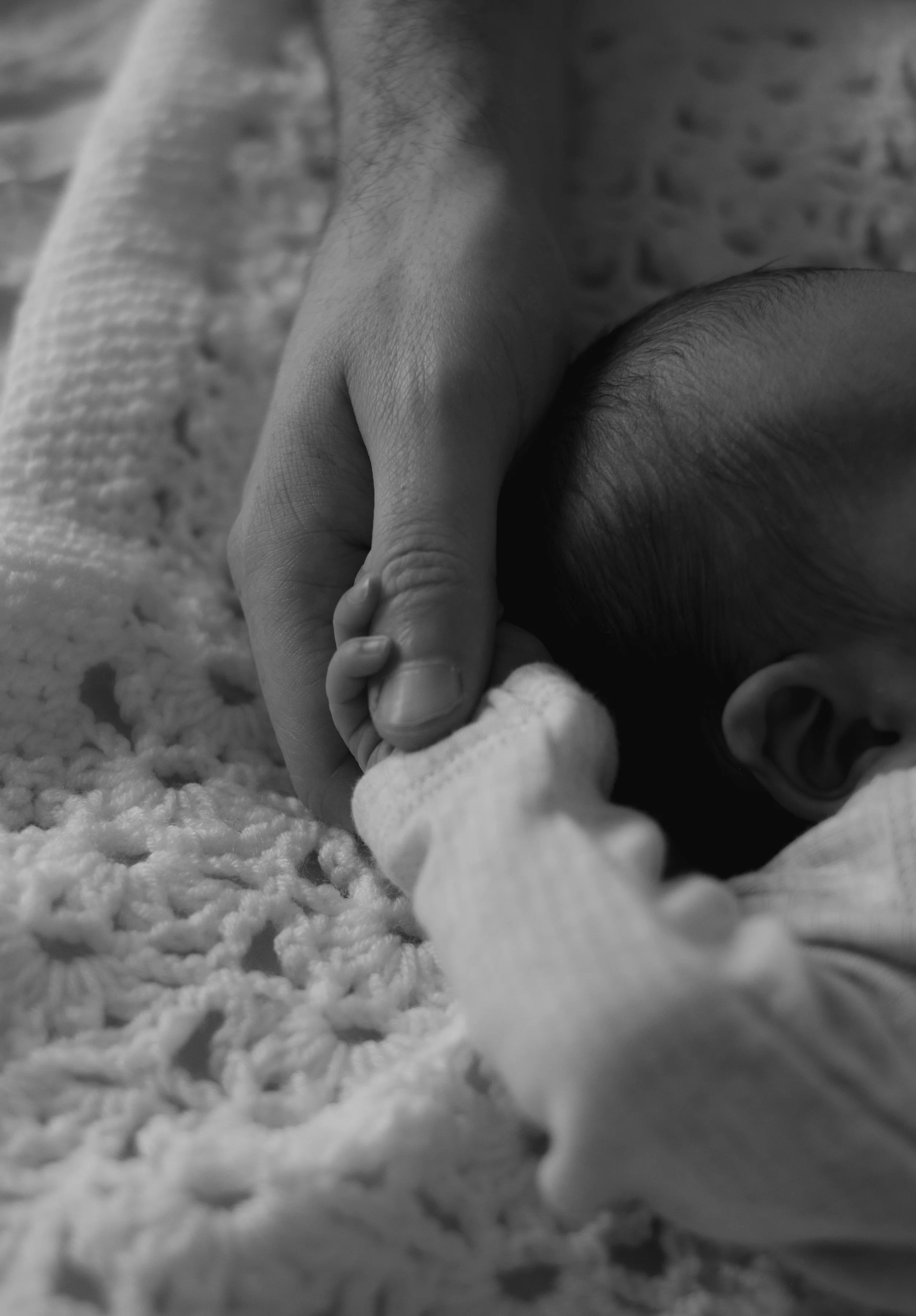 Close-up of an adult's hand holding a baby's hand, with both resting on a textured blanket.