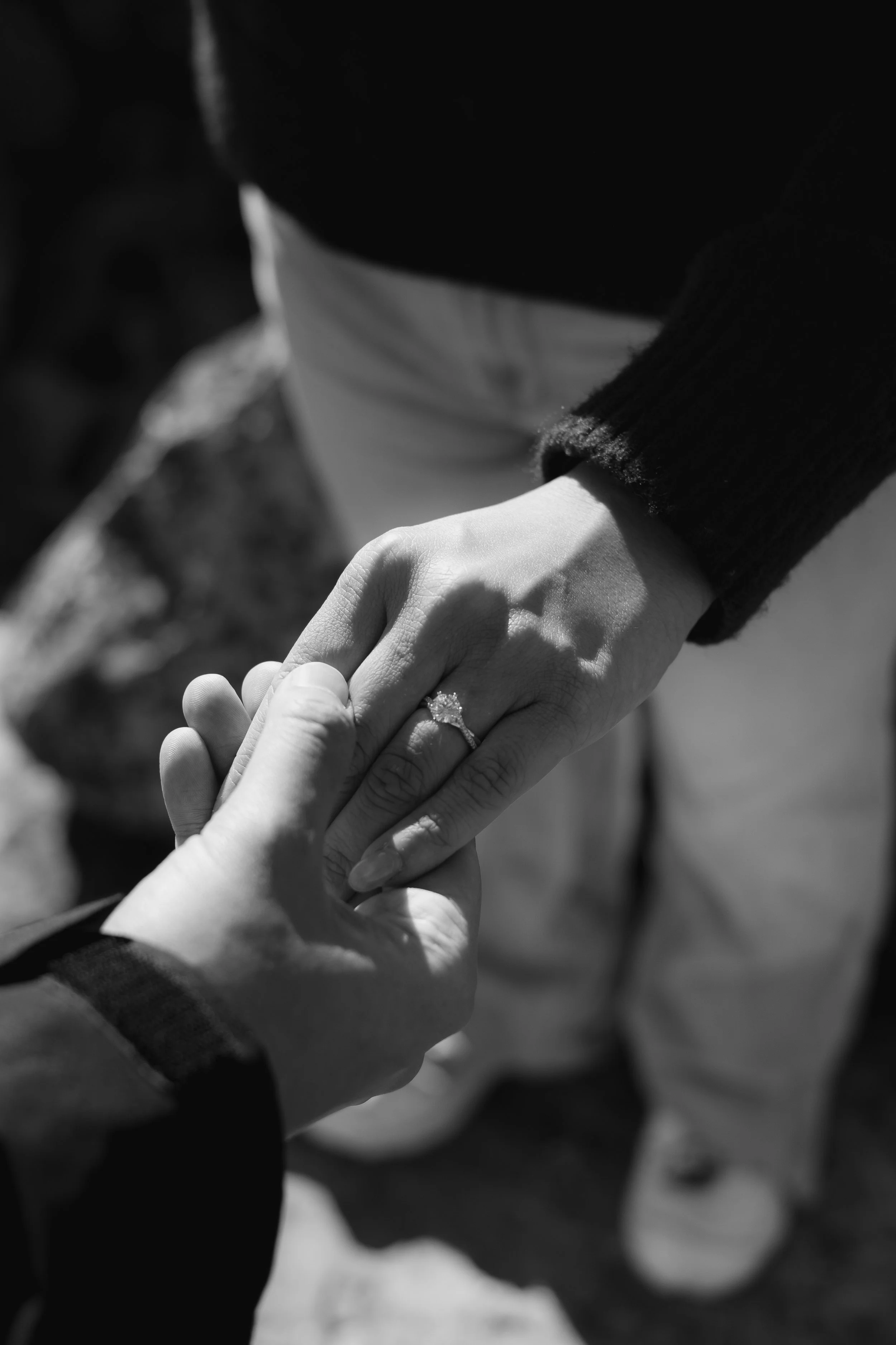 Close-up of two hands holding each other, with one person’s hand wearing a ring, in black-and-white photograph.