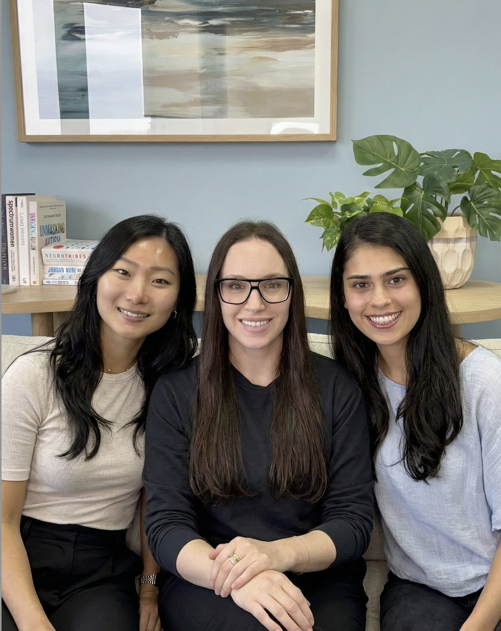 A woman sitting on a sofa in a room with a woven headboard and a pillow, smiling at the camera.
