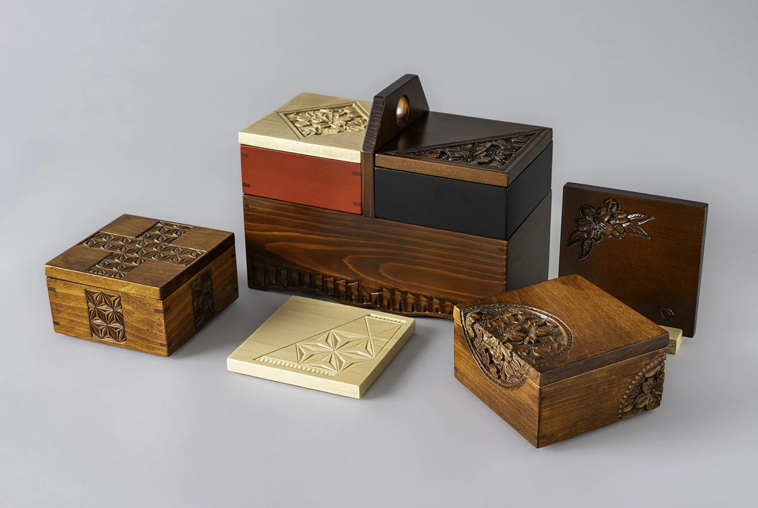 A collection of carved wooden boxes and tiles with intricate floral and geometric patterns, displayed on a plain surface.