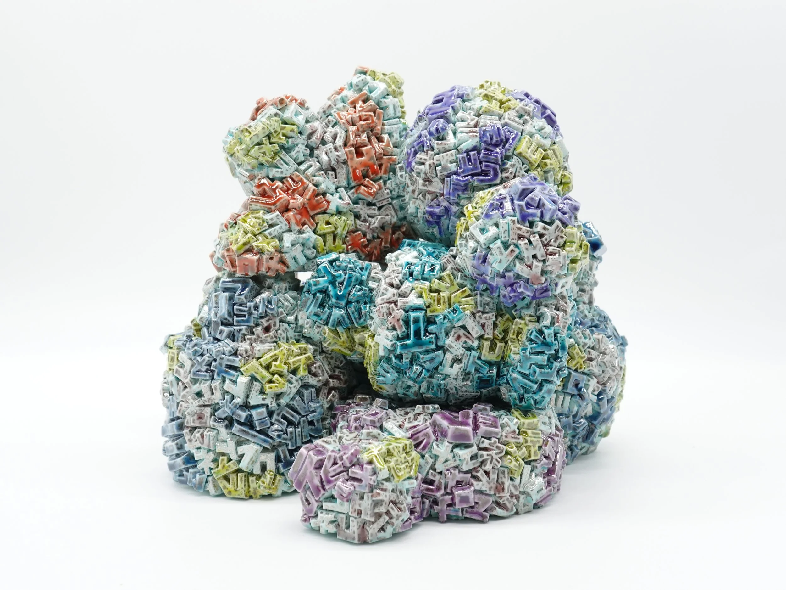 Colorful artistic sculptures made of small alphabet letter blocks stacked into rounded shapes on a white background.