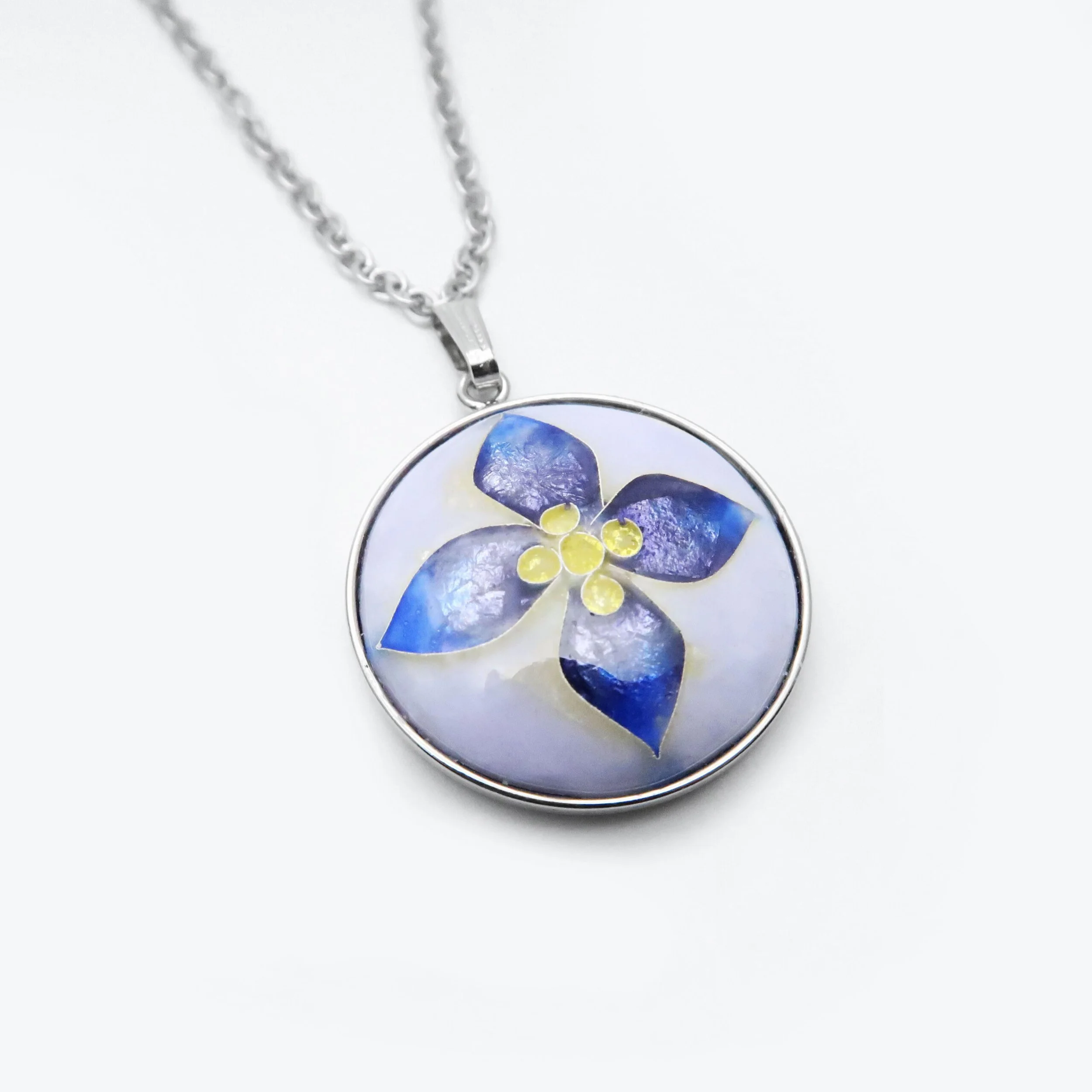 Round silver pendant necklace with a blue and yellow flower design inside.