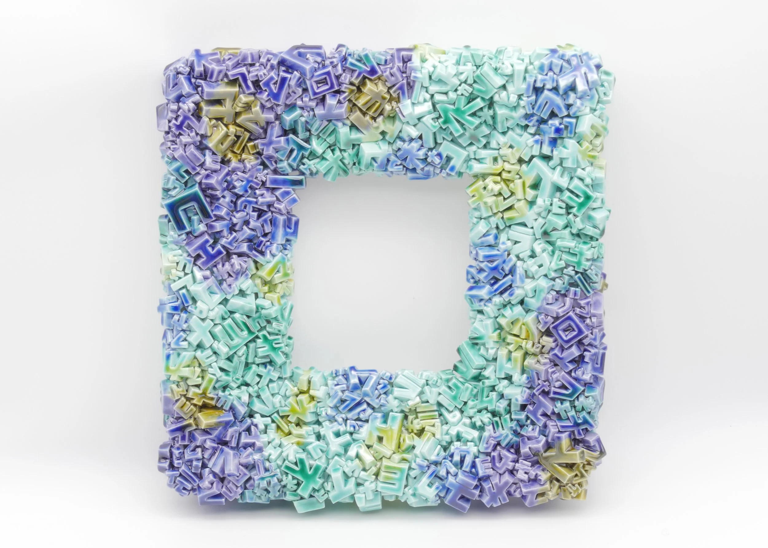 Colorful frame made of assorted plastic letters in pastel shades of purple, green, blue, and yellow, arranged in a square shape with a hollow center on a white background.