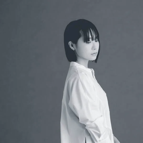 Black and white photo of a woman with shoulder-length hair, wearing a white shirt, looking thoughtfully to her left against a plain background.