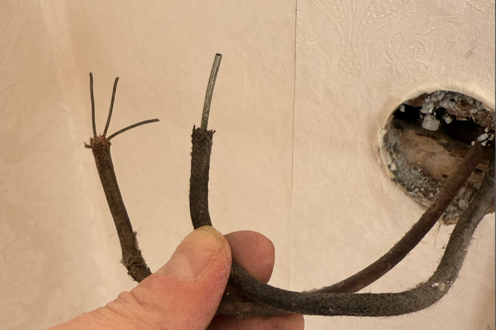 Exposed antique stranded and solid copper Knob and Tube wiring wrapped in degraded black cotton-cloth braiding, salvaged from a historic St. John's wall cavity.