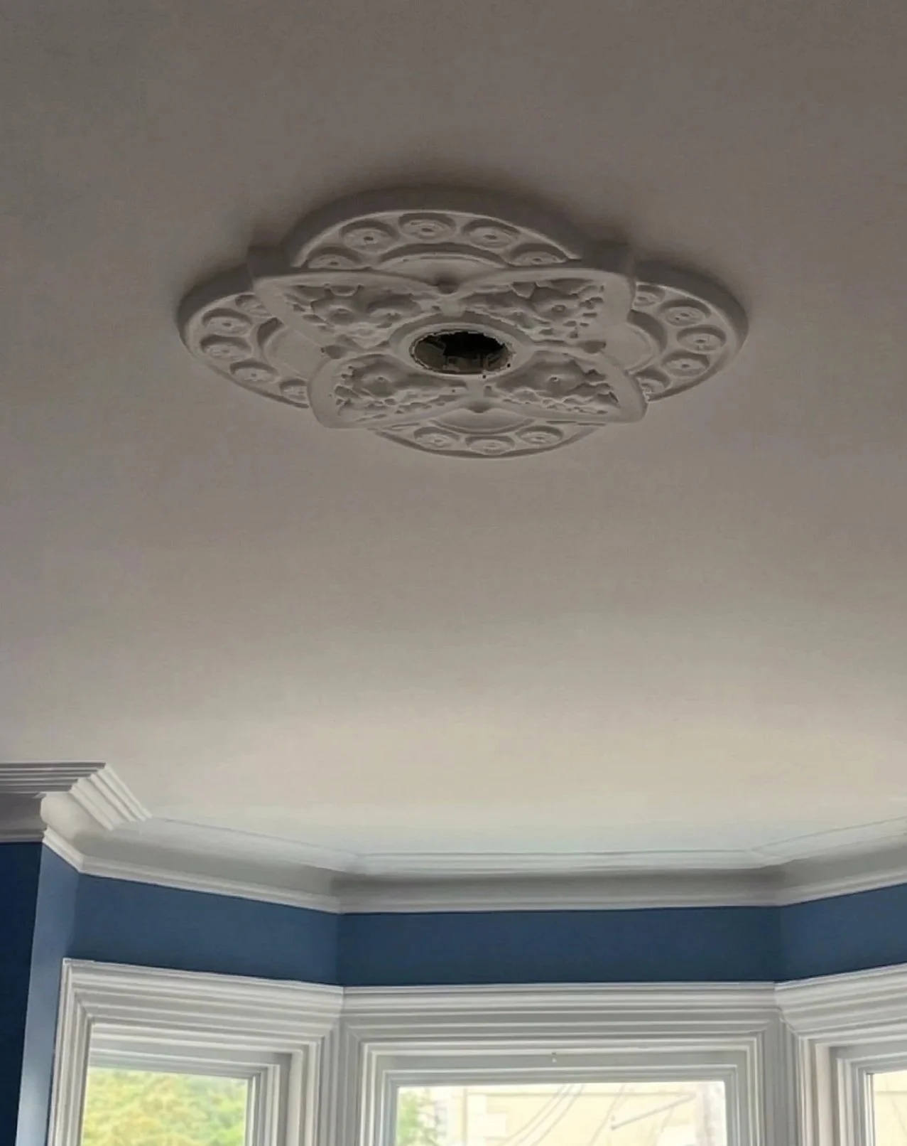 A beautifully preserved Victorian ornate plaster ceiling medallion centered above a bay window in a historic St. John's home. Originally designed to highlight grand 19th-century gas chandeliers (gaseliers) and protect ceilings from rising soot, these