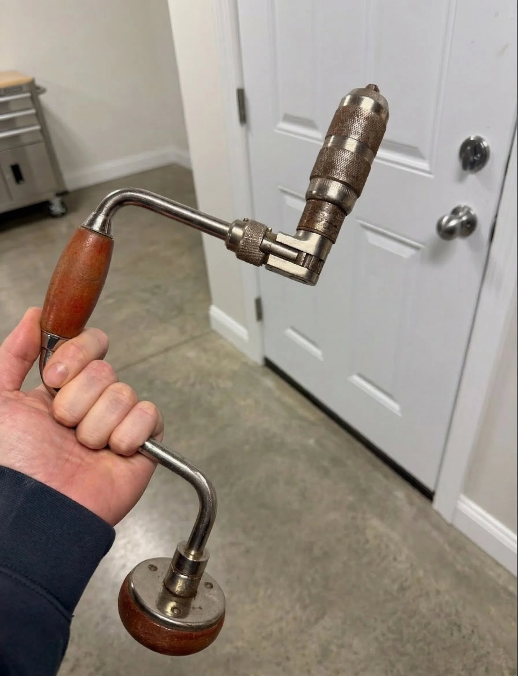 An antique early 20th-century electrician's "corner brace" hand tool, featuring angled bevel gears and wooden handles, historically used by tradesmen to manually bore wiring holes through thick old-growth timber inside tight wall cavities.