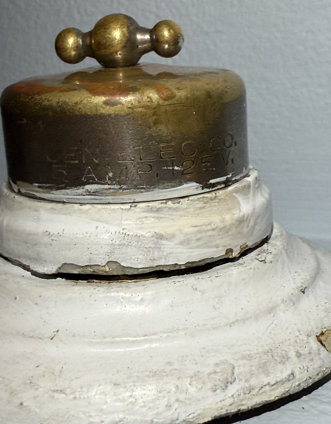 Close-up side profile of an antique GE "Barbell" rotary snap switch, highlighting the tarnished spun-brass dome resting on its thick fireproof porcelain insulator base.