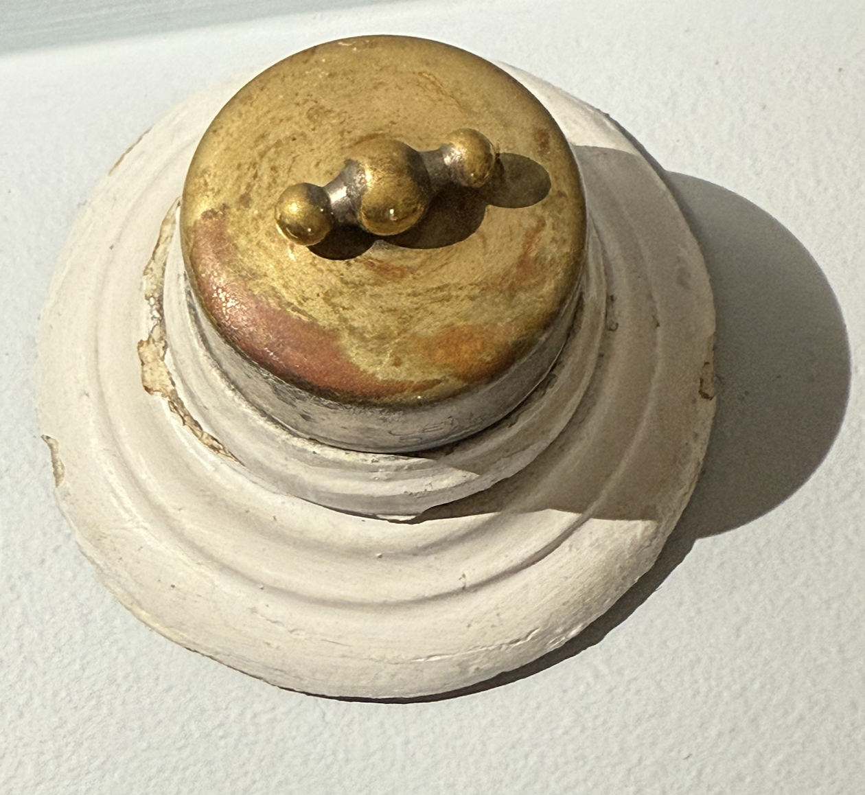 Top-down view of an early 1900s General Electric "Barbell" surface-mount rotary snap switch with a distinct solid-brass twisting handle on a painted porcelain base.