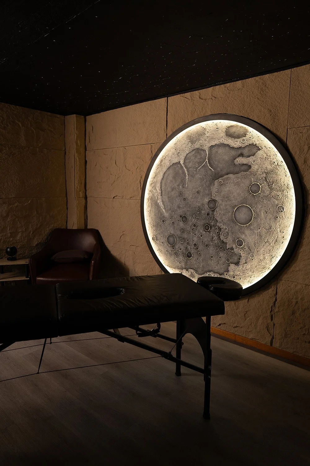 Sala de masaje en México con iluminación tenue, camilla y una gran instalación lunar como parte de un espacio sensorial.