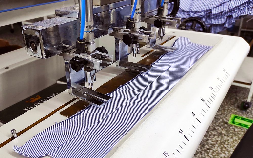 Automated sewing machine working on striped fabric, with precision tools and measurement markings visible.