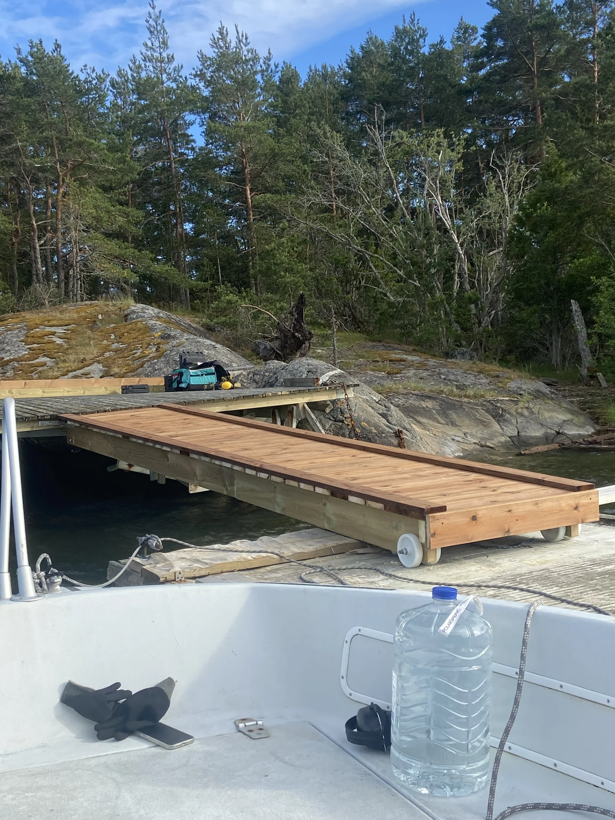 Wooden dock under construction by forested shoreline with tools and a small table on top.