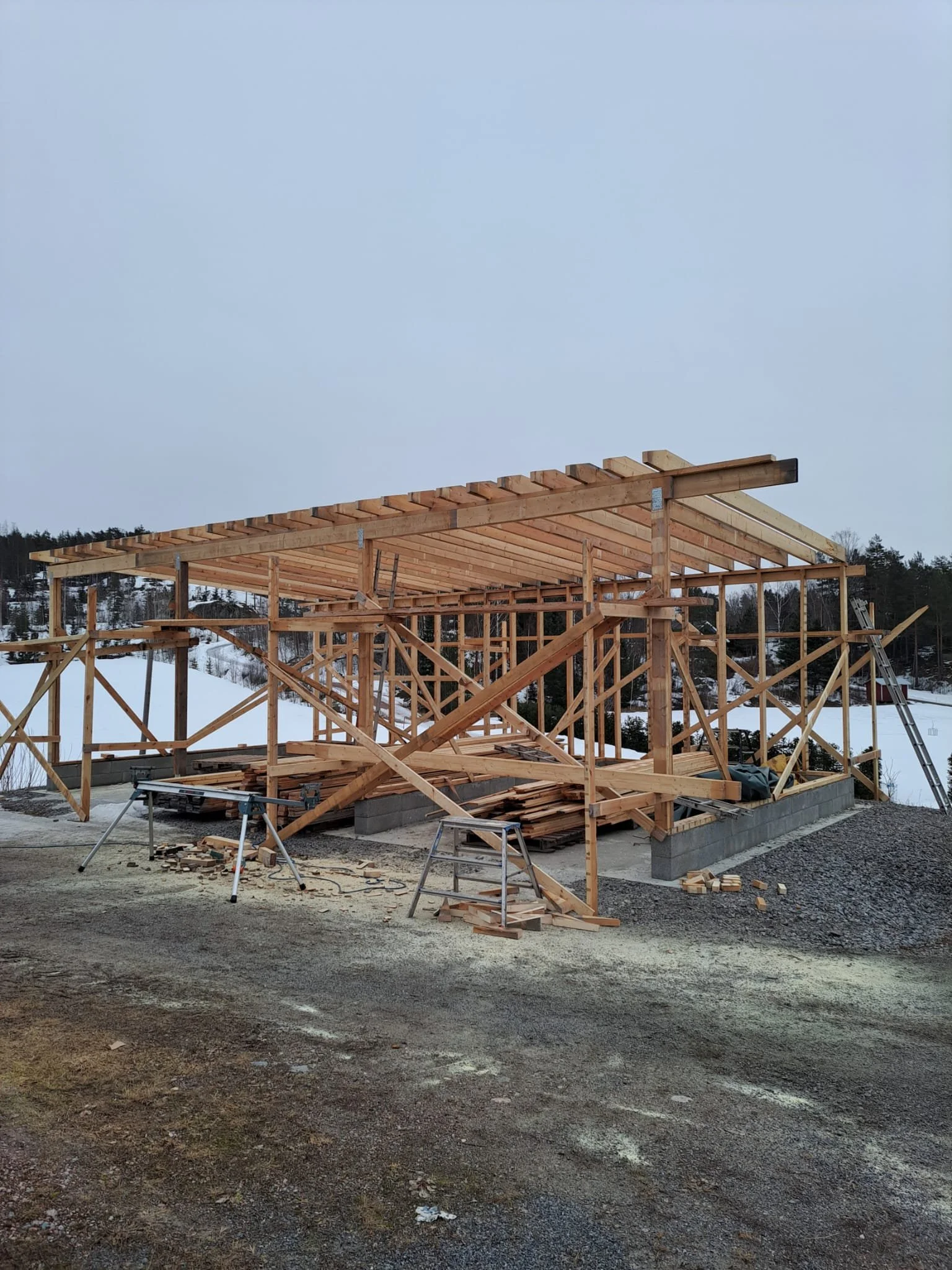 Wooden frame of a building under construction with sawhorses and building materials on the ground.