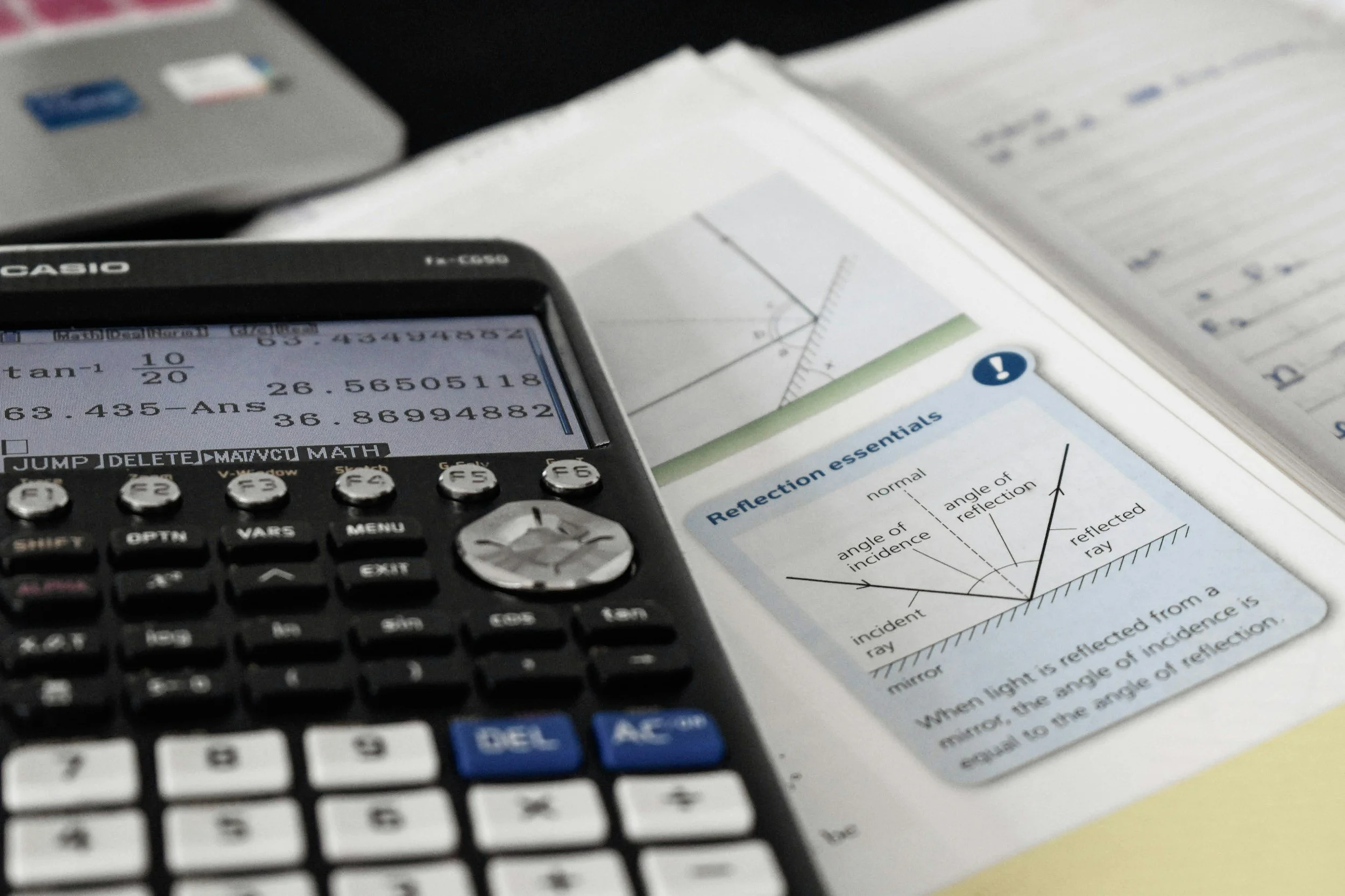 A calculator, textbooks with a graph, and a note on reflection of light with diagram and instructions.