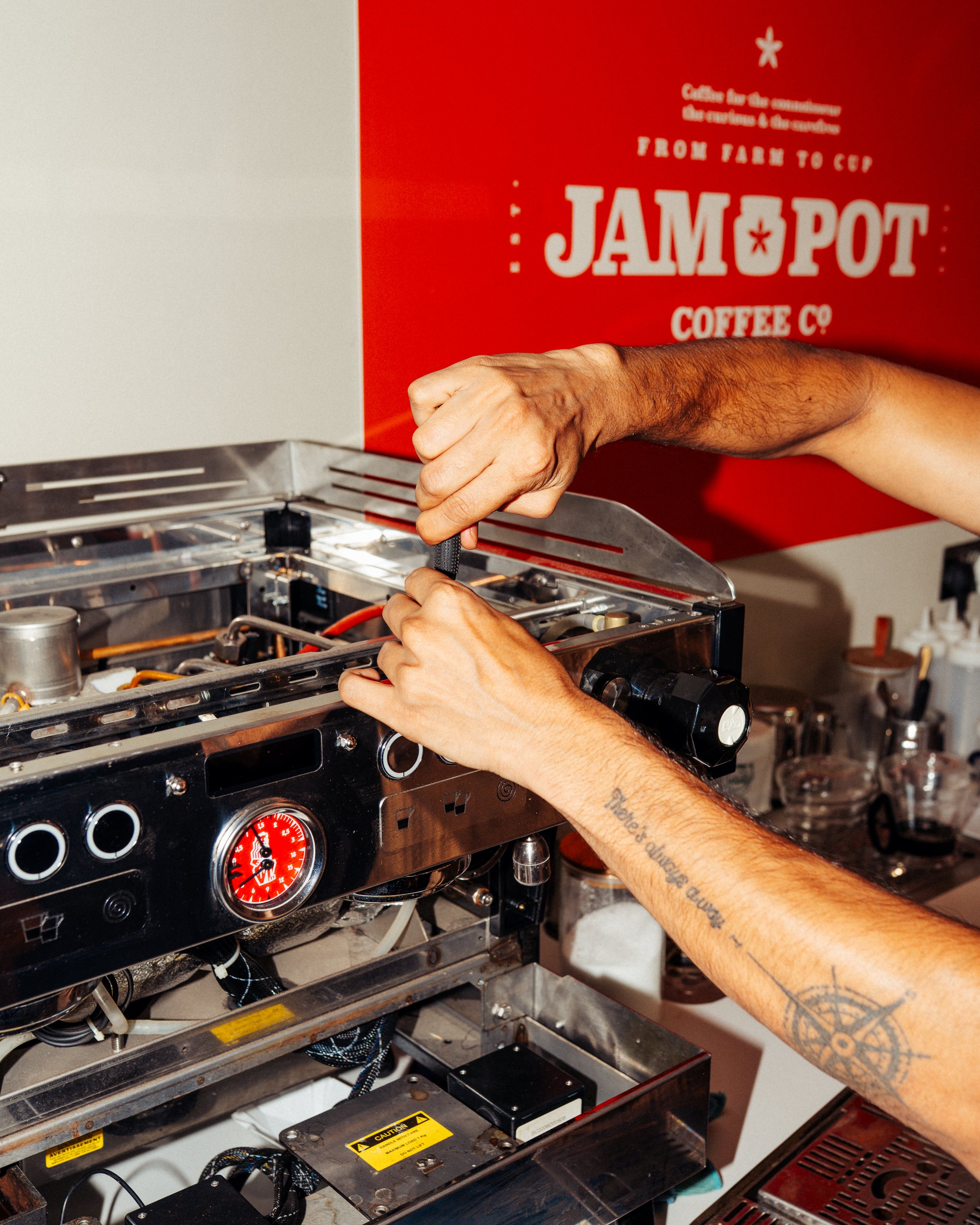 Person working on a coffee machine with the Jampot Coffee Co sign in the background.