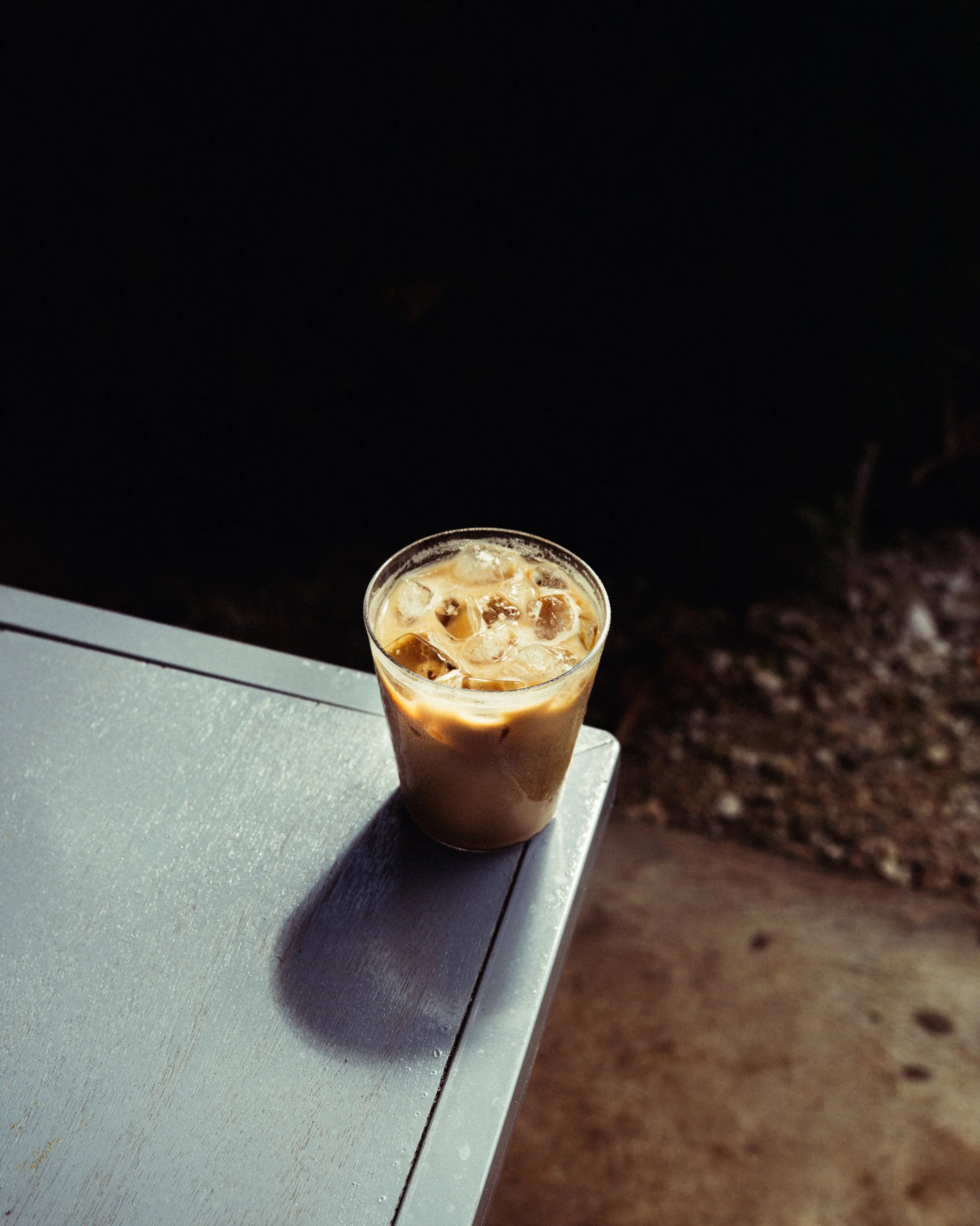 A glass of iced coffee on a table, with ice cubes visible inside, on a dark outdoor setting at night.