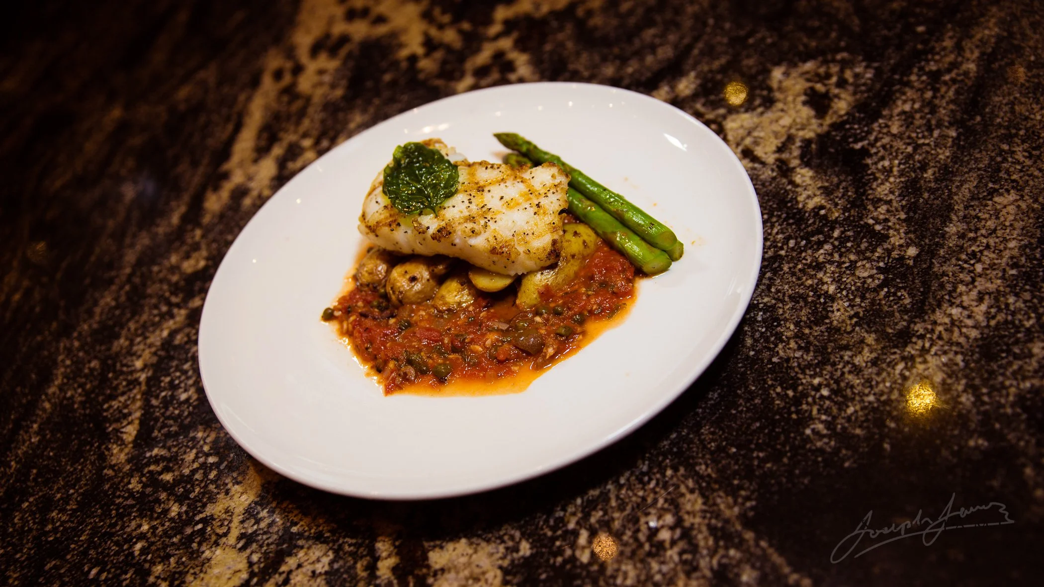 Grilled fish with asparagus and tomato sauce on a white plate.