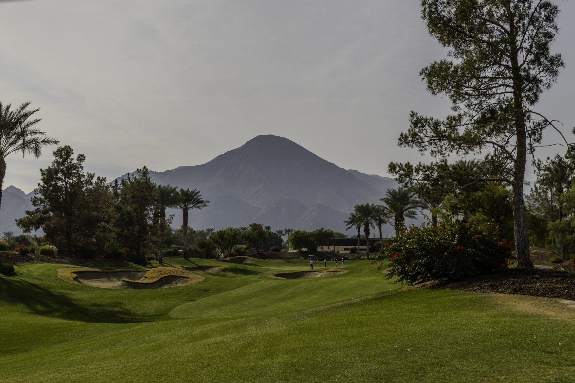 Golf course with hills and palm trees under a cloudy sky