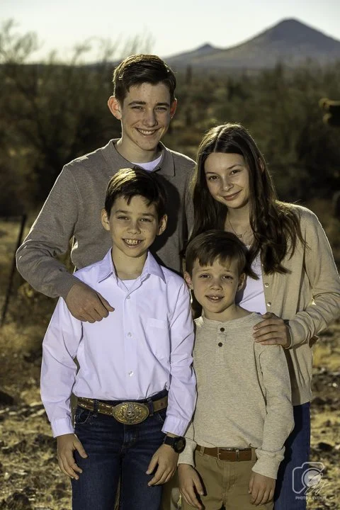 Four children posing outdoors with a desert landscape and mountains in the background.