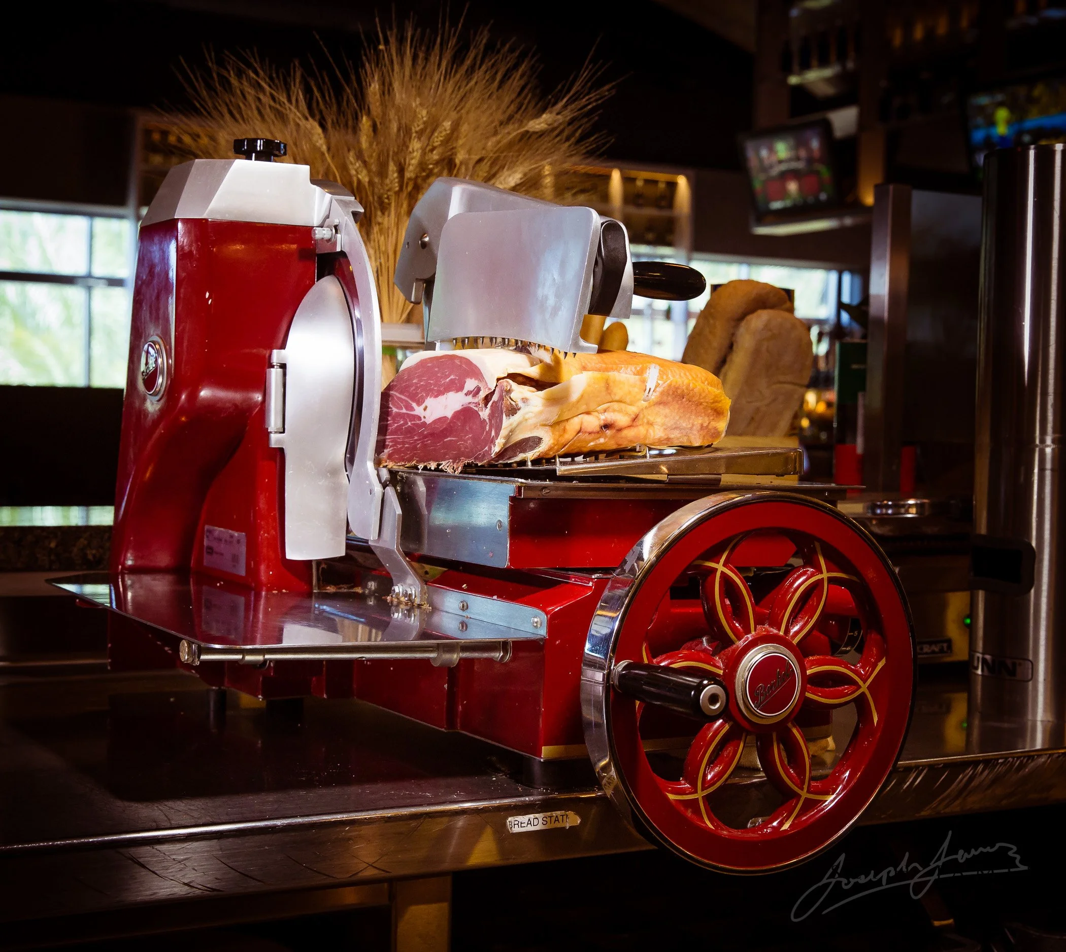 Vintage red meat slicer with prosciutto and bread in a restaurant setting.
