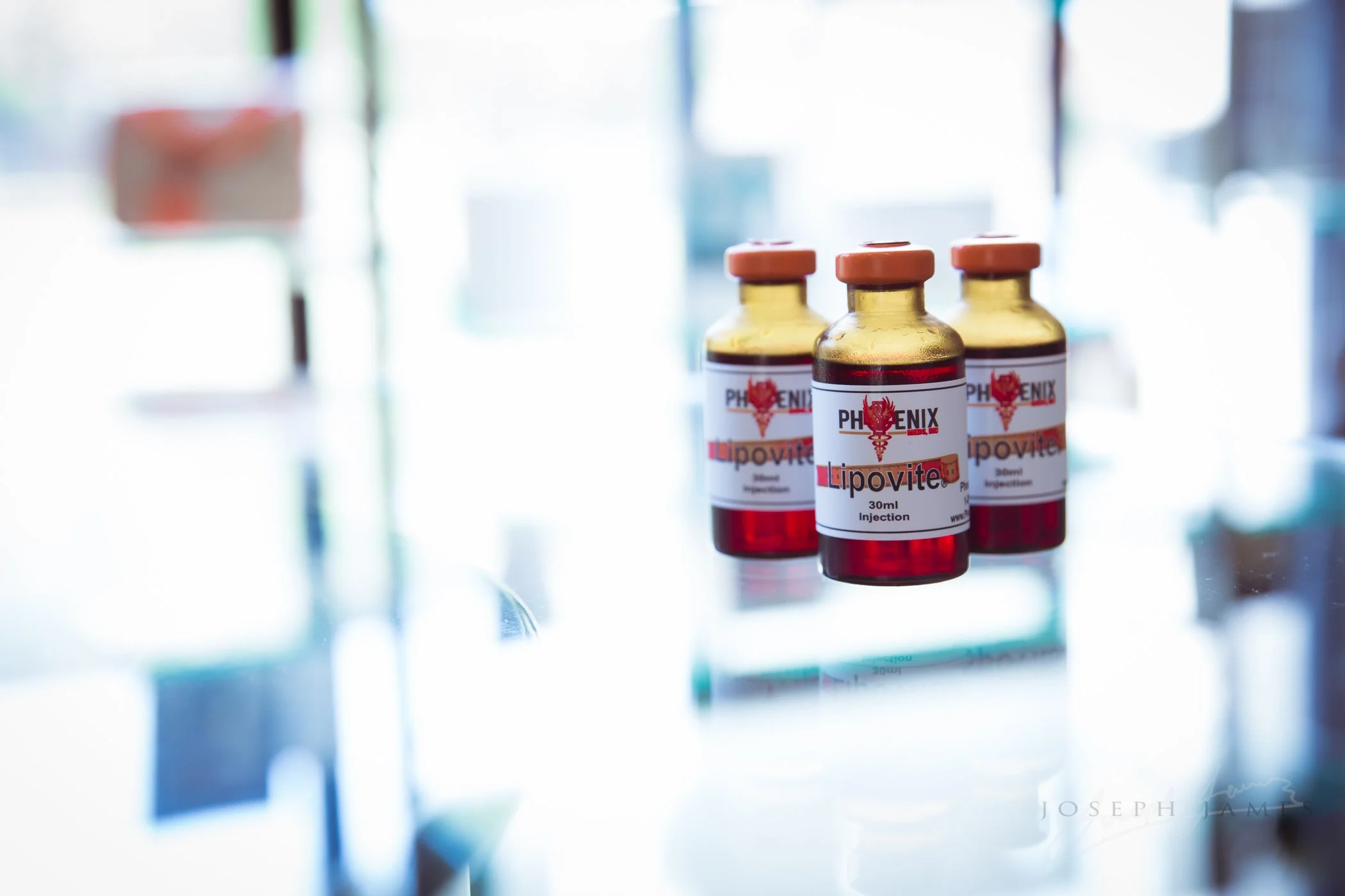 Three glass vials labeled "Phoenix Lipovite 30ml Injection" with orange caps on a reflective surface.