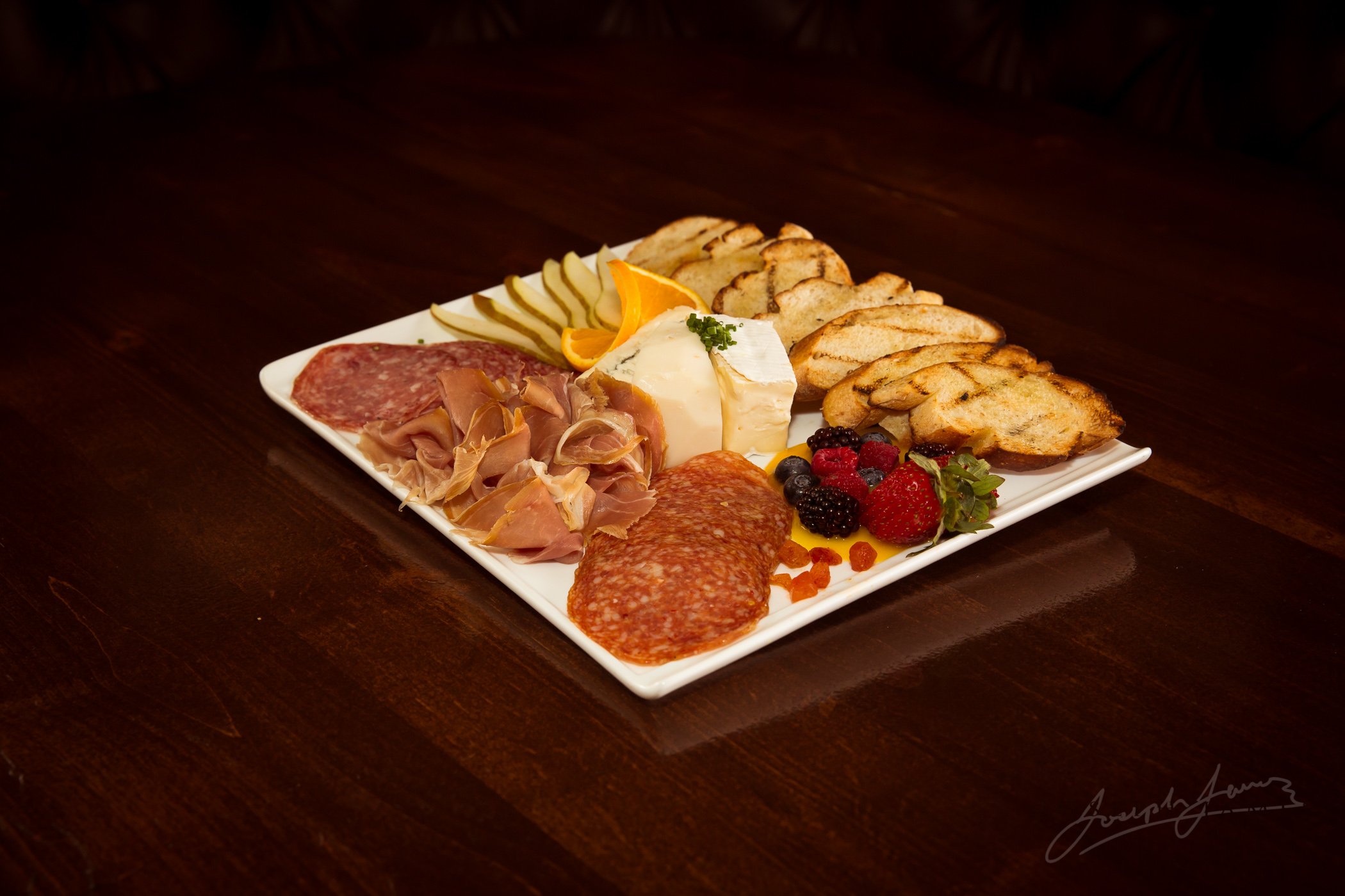 Charcuterie board with assorted meats, cheese, bread, fruits, and condiments.