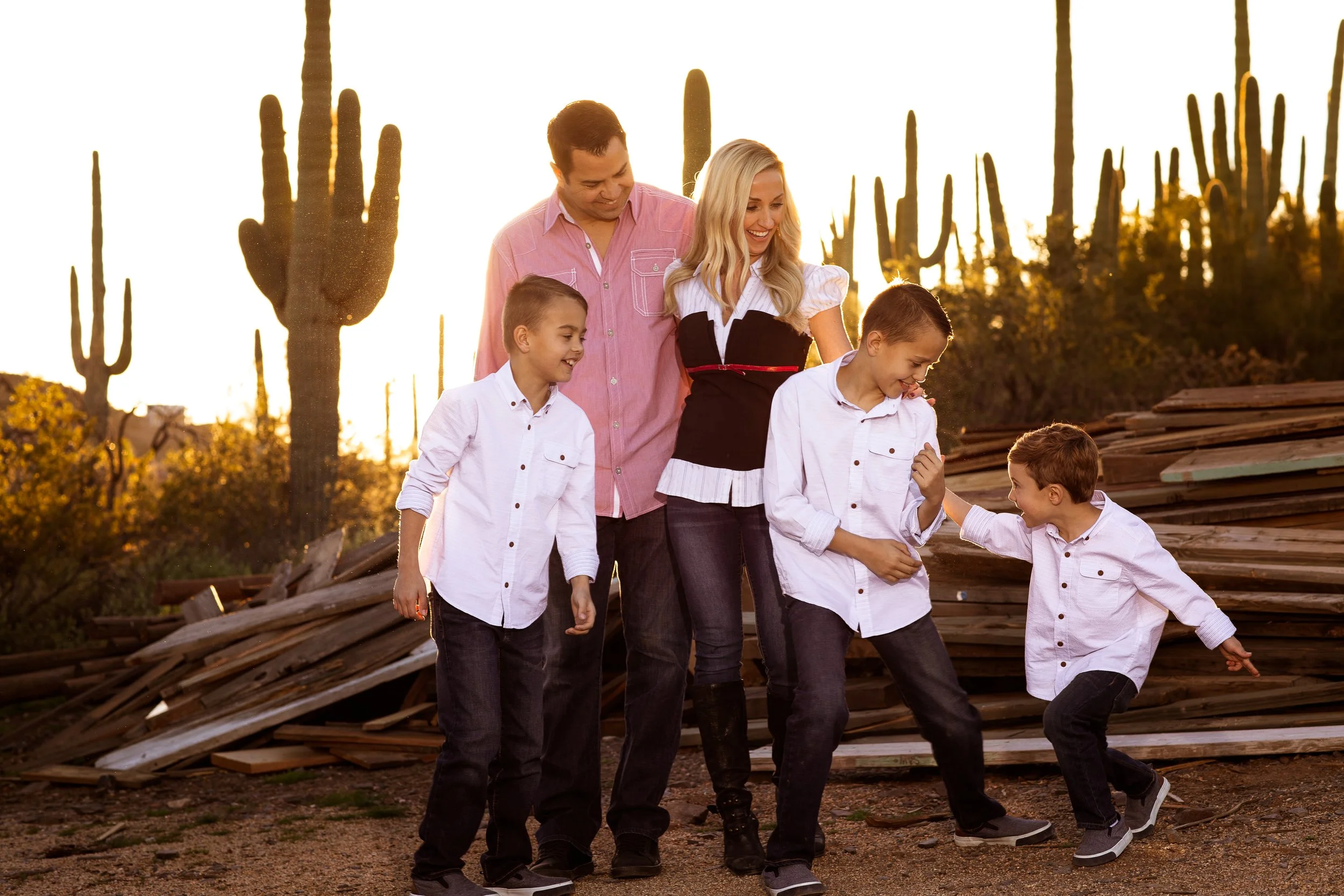 Family with three children laughing in a desert setting with cacti and wood piles in the background.
