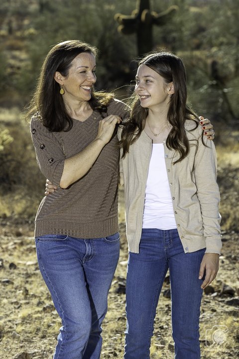 Mother and daughter smiling in a desert landscape with a cactus in the background.