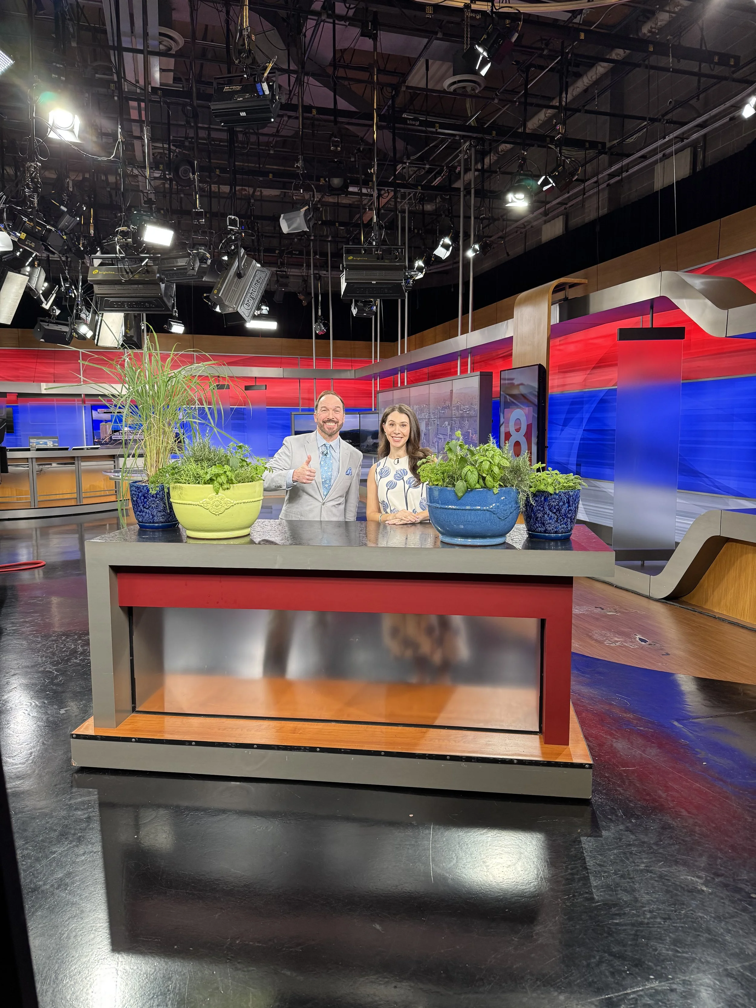 News Studio Man and Woman standing behind counter with planters of green plants