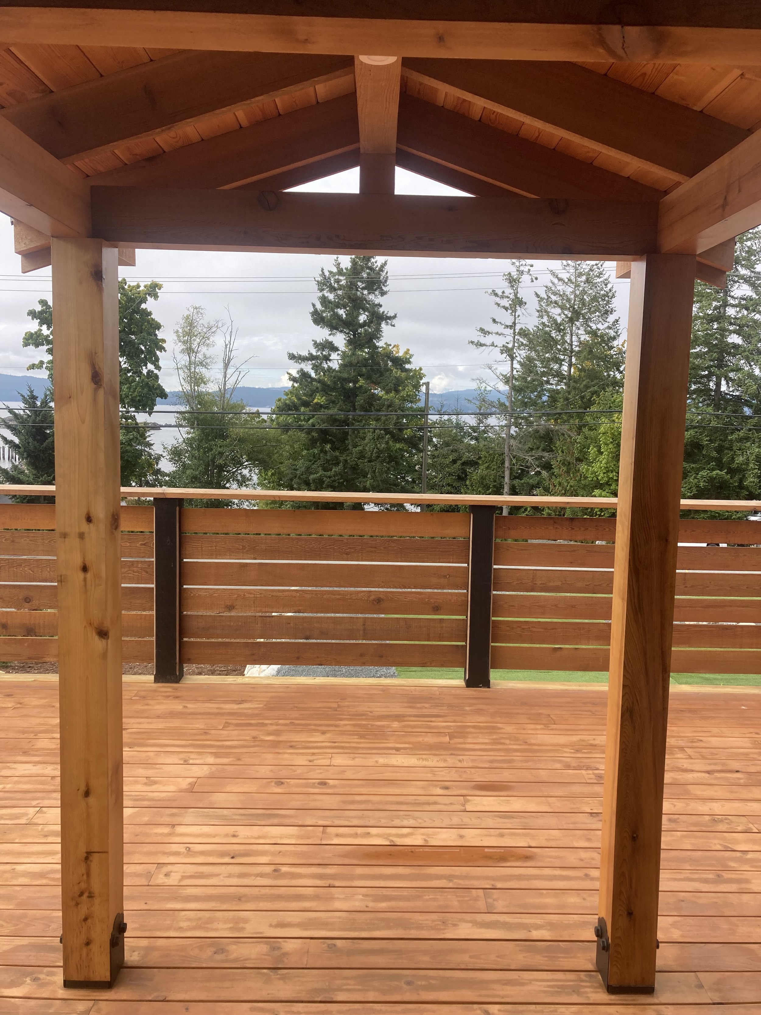 Wooden deck with overhang, trees in the background, and a view of a body of water.