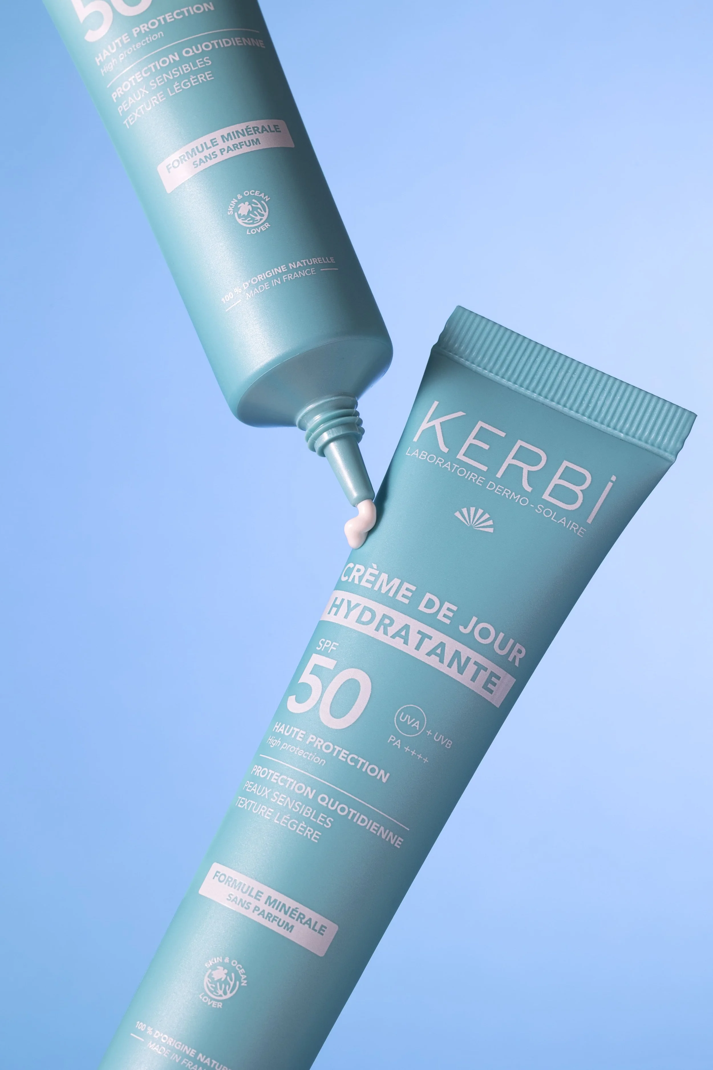 Tube de crème hydratante de jour Kerbi avec SPF 50, placé sur un fond bleu, avec une partie de la crème sortant du tube.