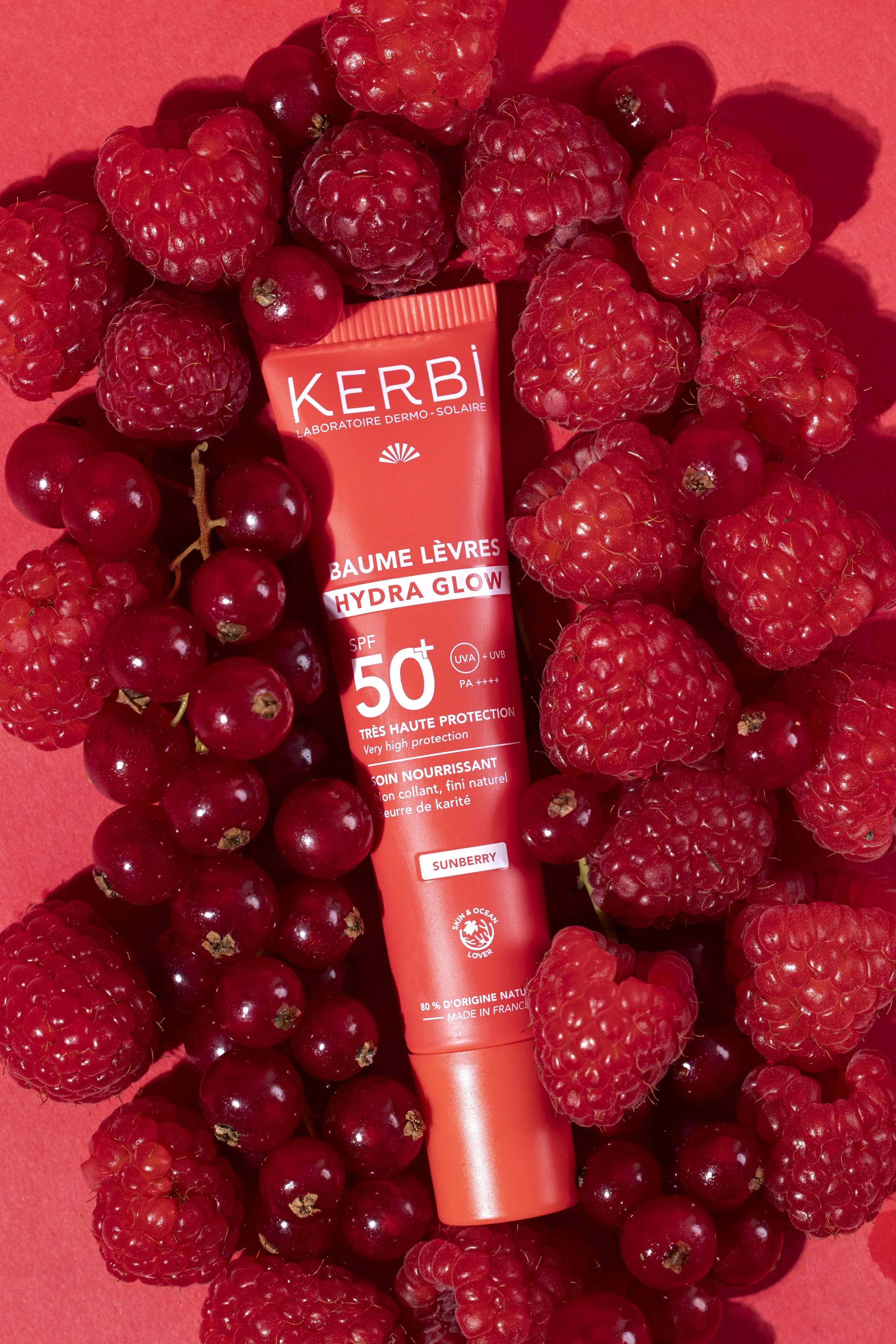 Un tube de baume à lèvres rouge entouré de mûres et de groseilles rouges sur un fond rouge.