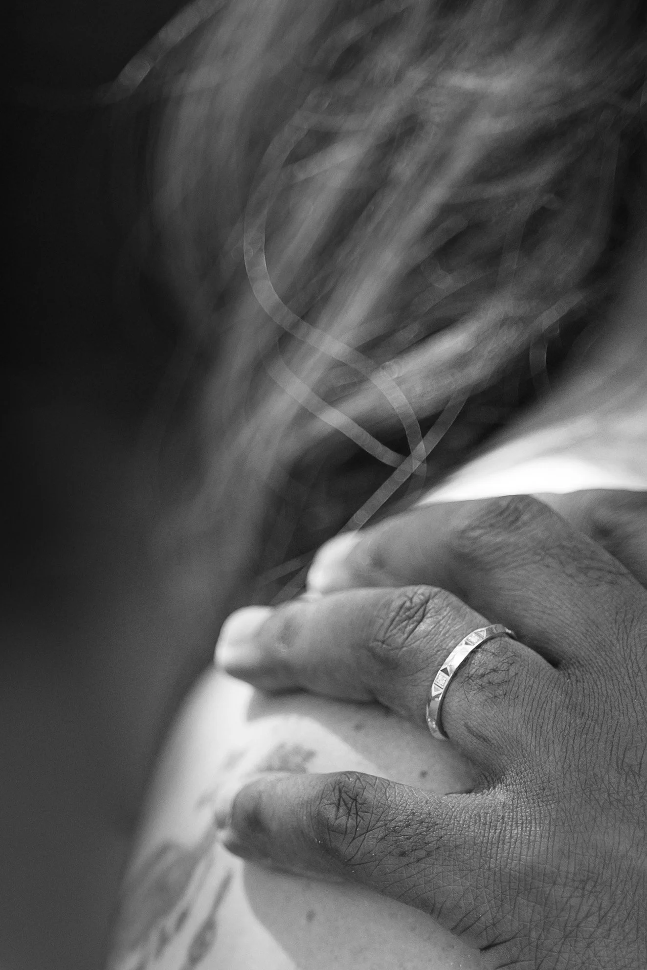 Main d'une personne avec une bague, tenant ou touchant sa poitrine, en noir et blanc.