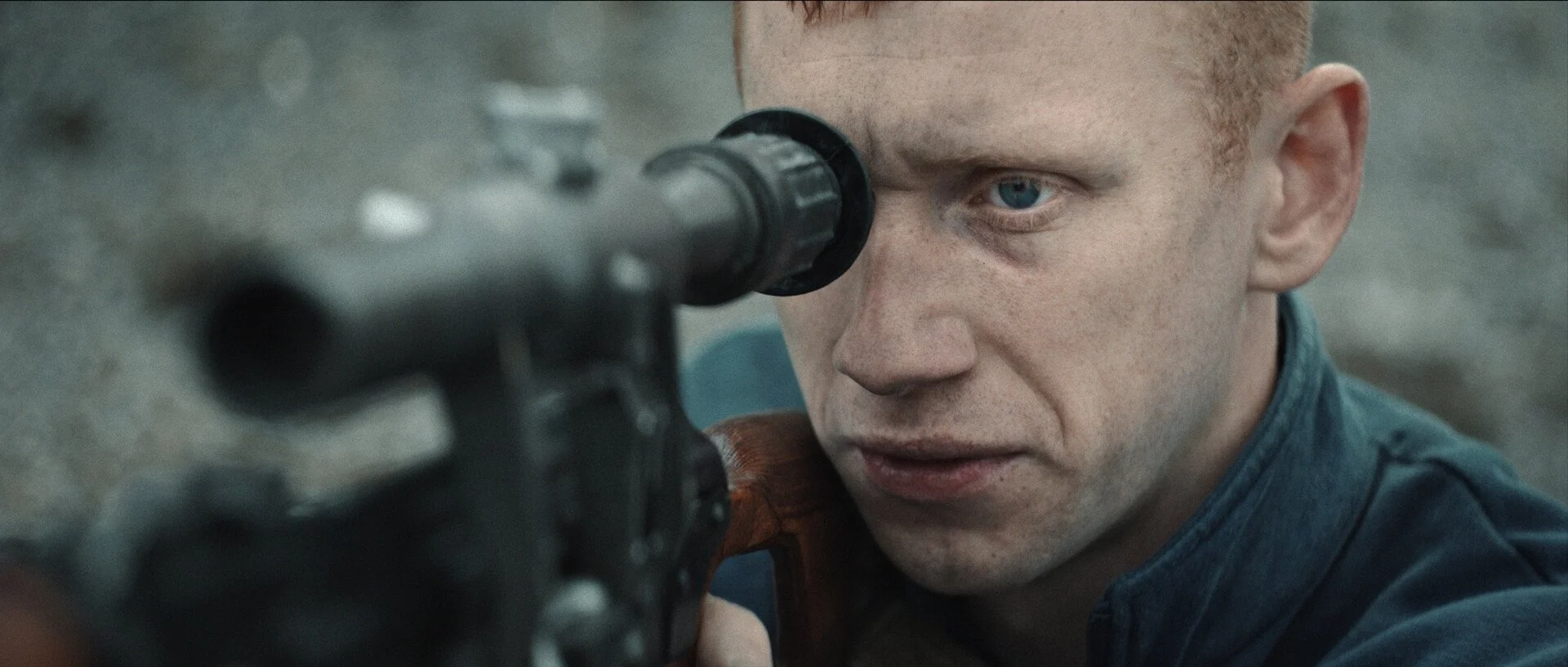 Close-up of a man with blue eyes aiming a rifle through the scope.