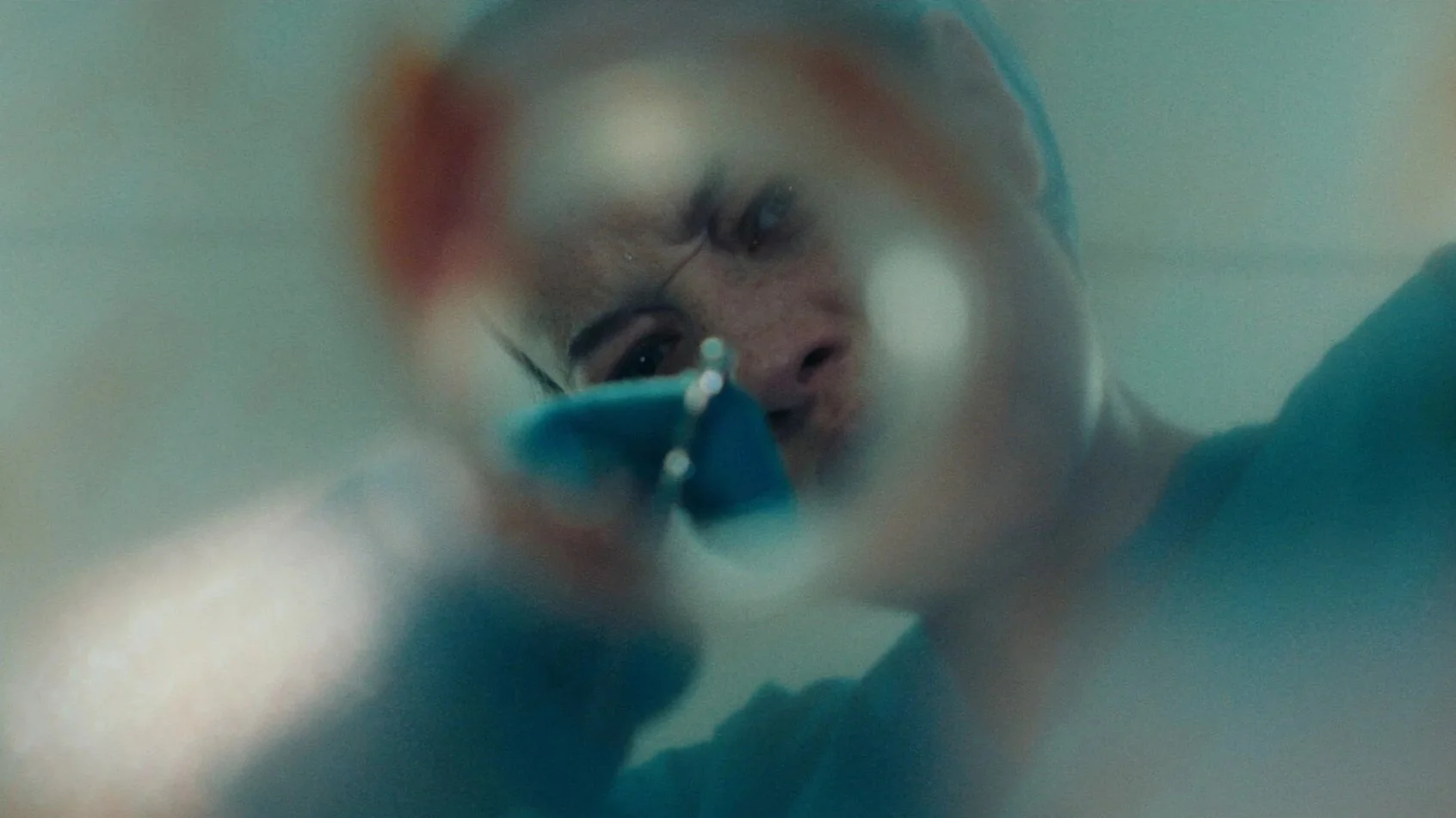 Close-up of a woman with glasses holding a blue object, viewed from below, with her face partially obscured.