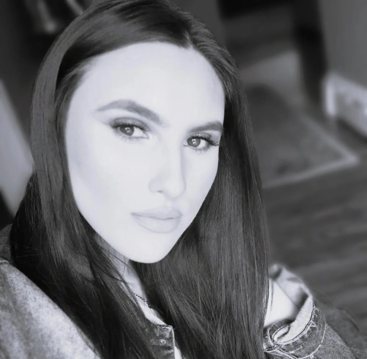 Black and white portrait of a woman with long, dark hair, wearing a denim jacket, looking at the camera.