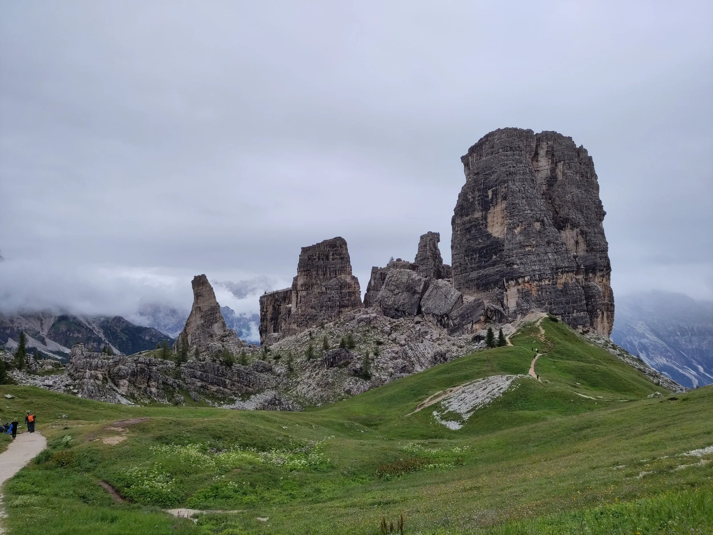 A scenic view of tall, rugged mountain formations with green grassy foreground and a cloudy sky in the background.